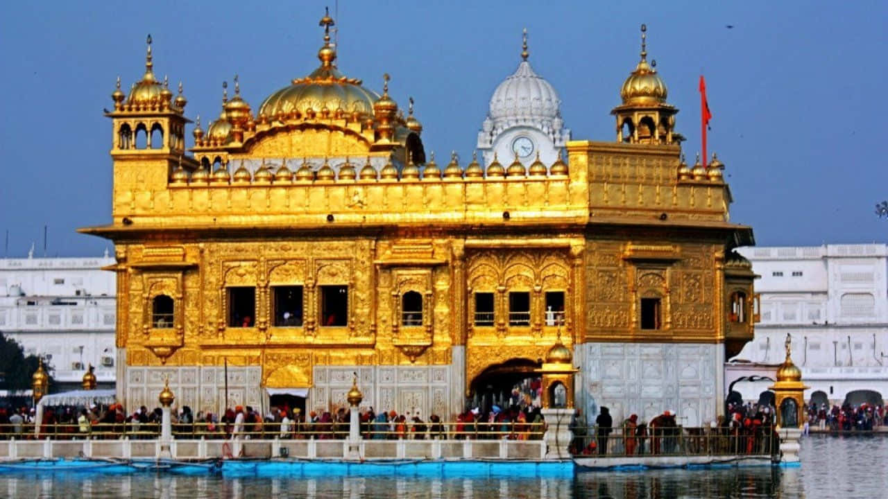 Golden Temple 桌布 壁紙 — 金色寺廟在清澈藍天下閃耀，信徒聚集在其神聖水池周圍，水池倒映出宏偉的建築。