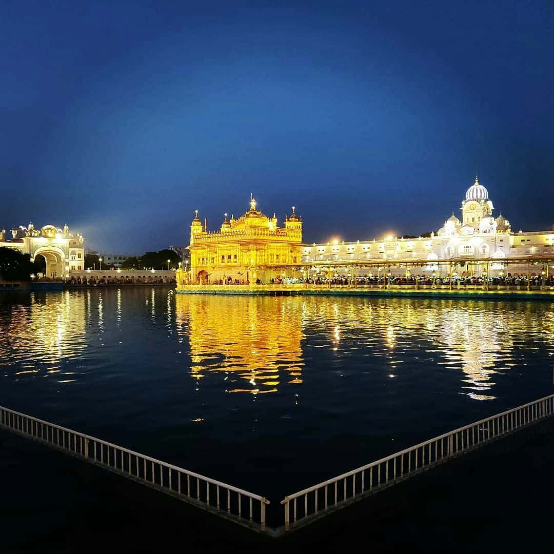 Golden Temple 桌布 壁紙 — 金色寺廟在黃昏時分被溫暖的燈光照亮，在深藍色天空下平靜的水面上反射。