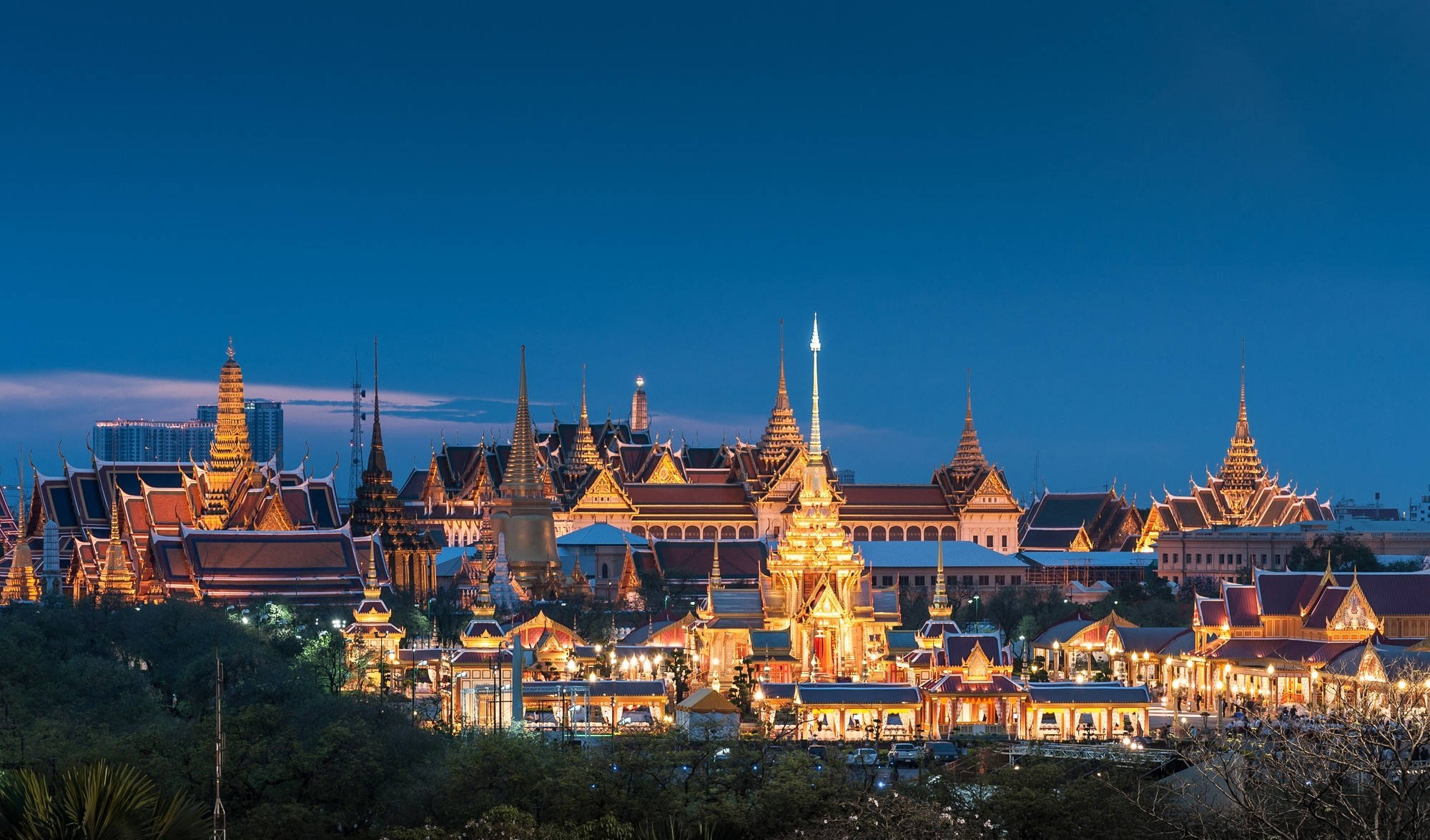 Bangkok 桌布 壁紙 — 金色寺廟尖塔在深藍色暮色天空下溫暖地閃耀，坐落於廣闊的皇家建築群中。