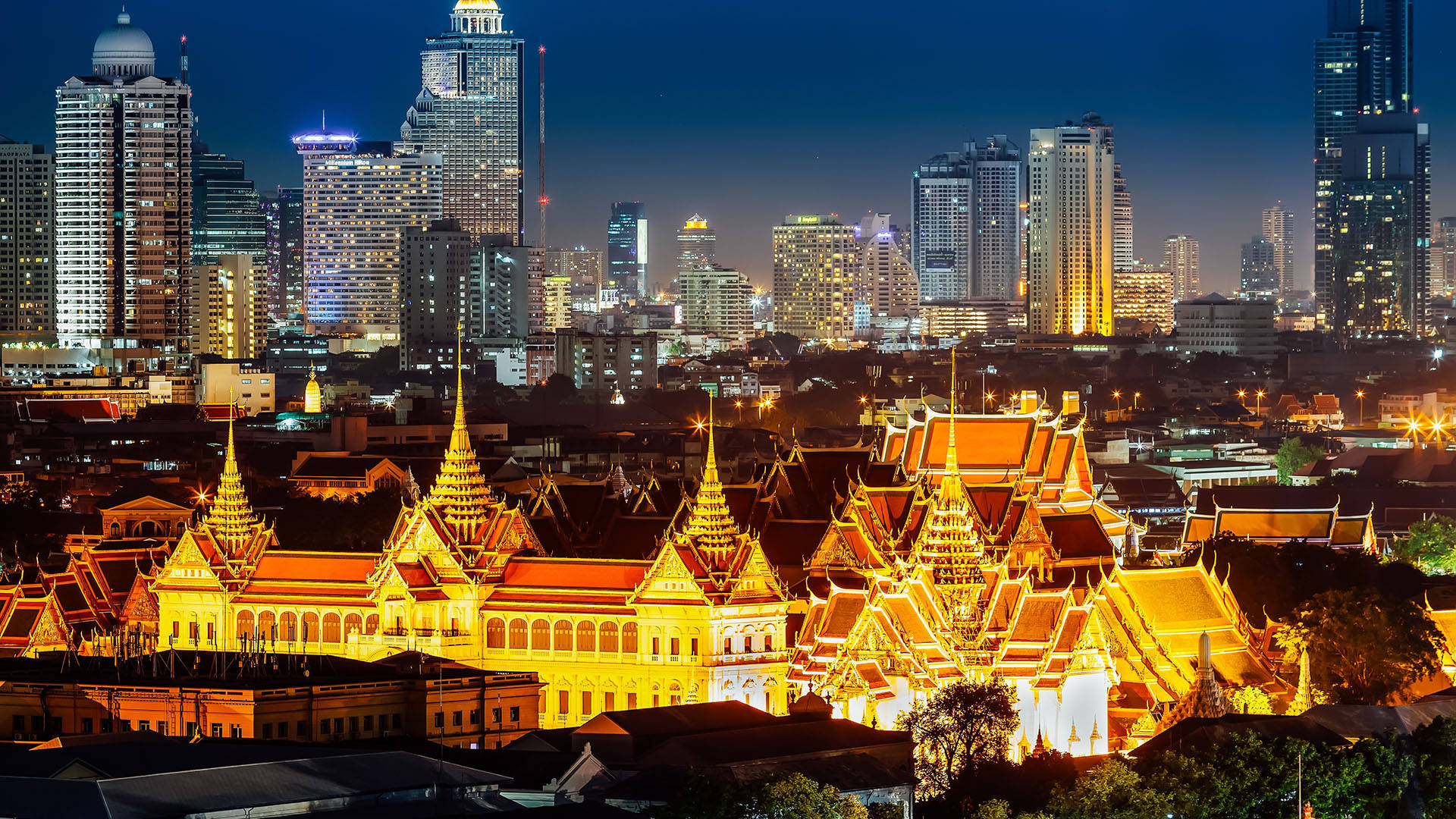 Bangkok 桌布 壁紙 — 金色寺廟尖頂在深藍色夜空下溫暖地發光，與被城市燈光照亮的現代摩天大樓形成對比。