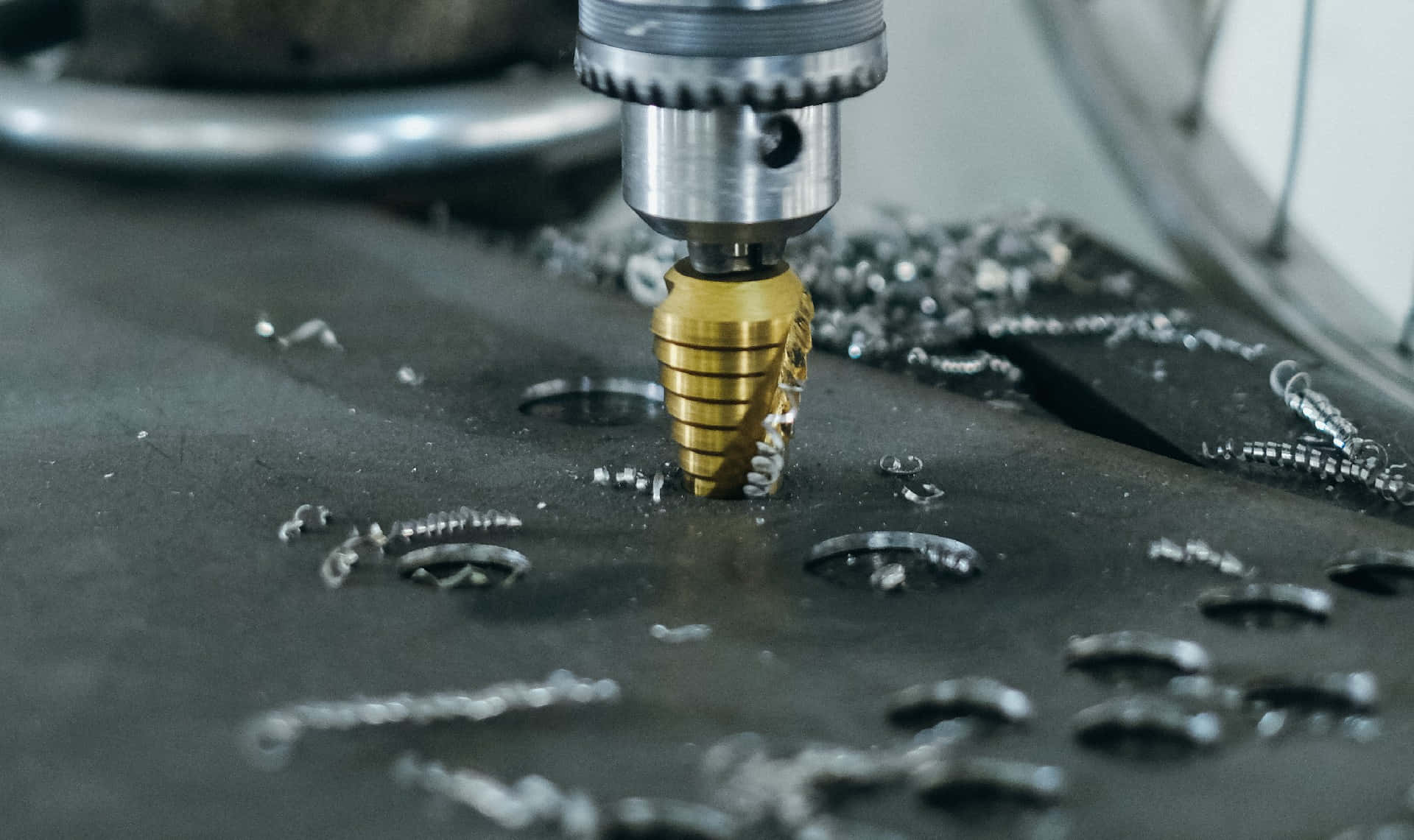 drill 桌布 壁紙 — 金色尖端鑽頭在深色金屬上精確鑽孔的近距離特寫，周圍散落著閃亮的金屬碎屑。