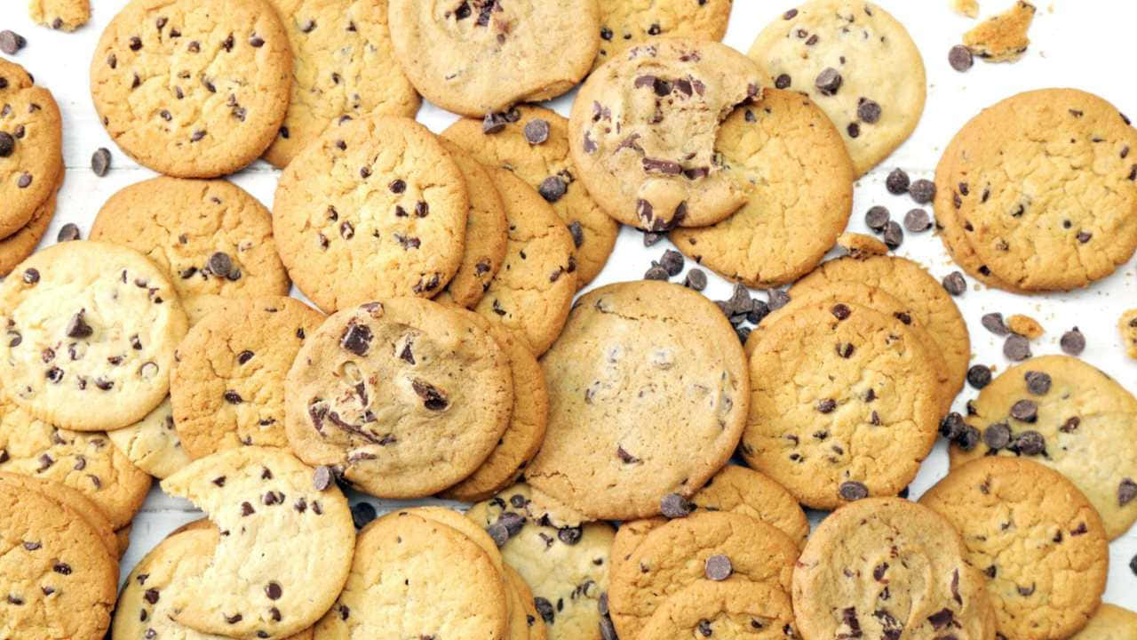 720p Cookies 桌布 壁紙 — 金色巧克力餅乾散落在白色表面上，並有鬆散的巧克力碎片的特寫。