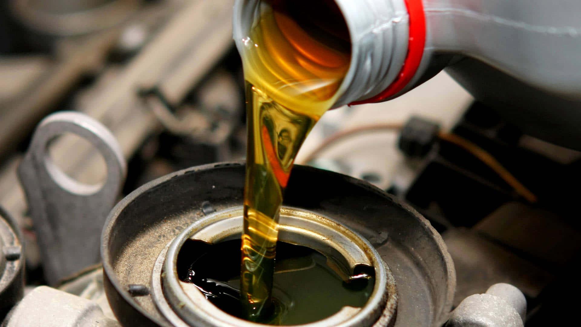 Oil 桌布 壁紙 — 金色引擎機油從瓶子平穩地倒入開放的引擎曲軸箱，背景中的金屬部件模糊不清。