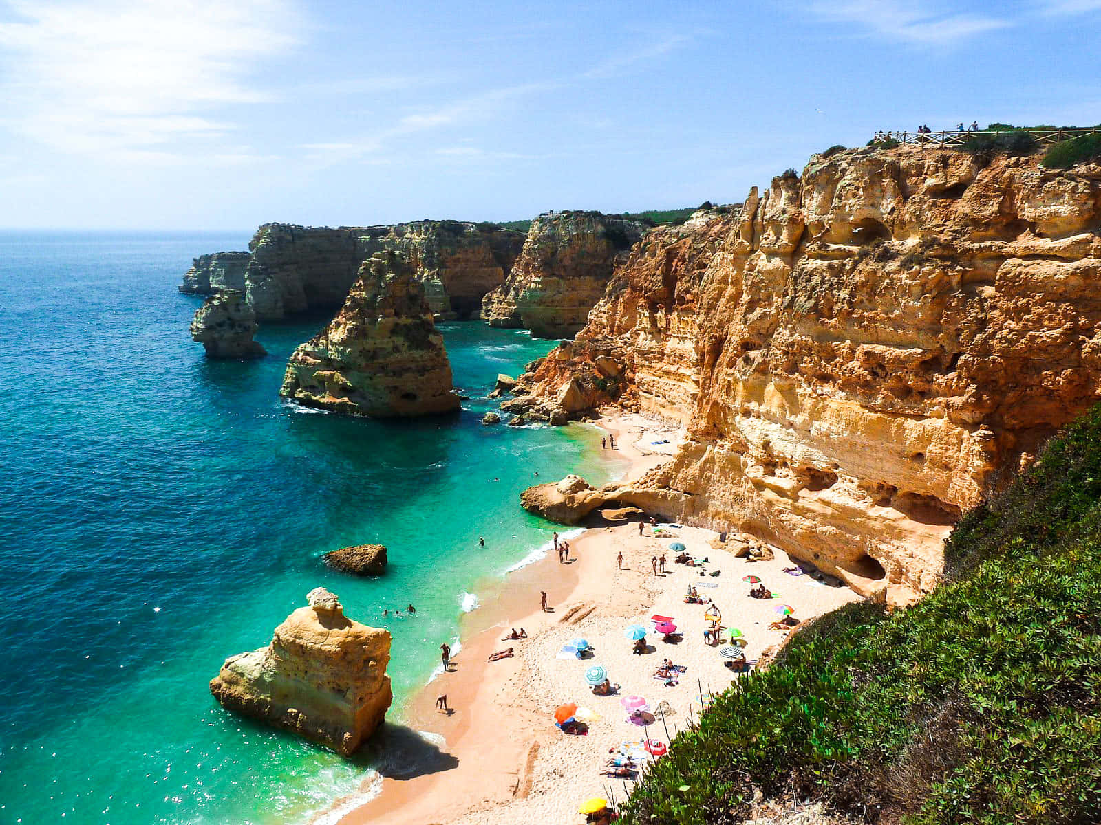 Portuguese Beach 桌布 壁紙 — 金色懸崖之間充滿活力的藍綠色海灣，沙灘上有色彩繽紛的遮陽傘和享受日光浴的人們。