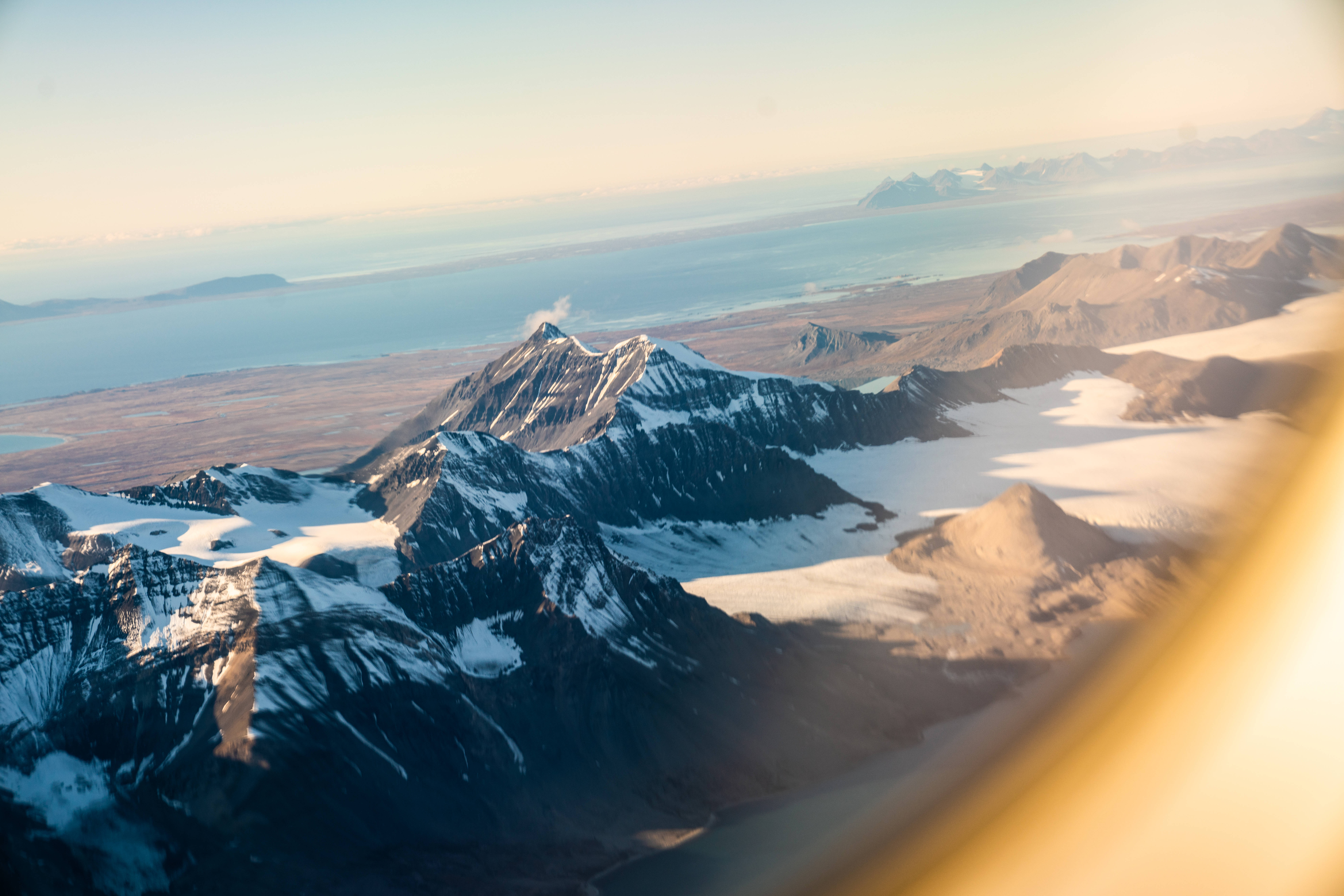 Svalbard 桌布 壁紙 — 金色日出光芒下，廣闊海洋旁邊的雪山和冰川的航拍視圖。