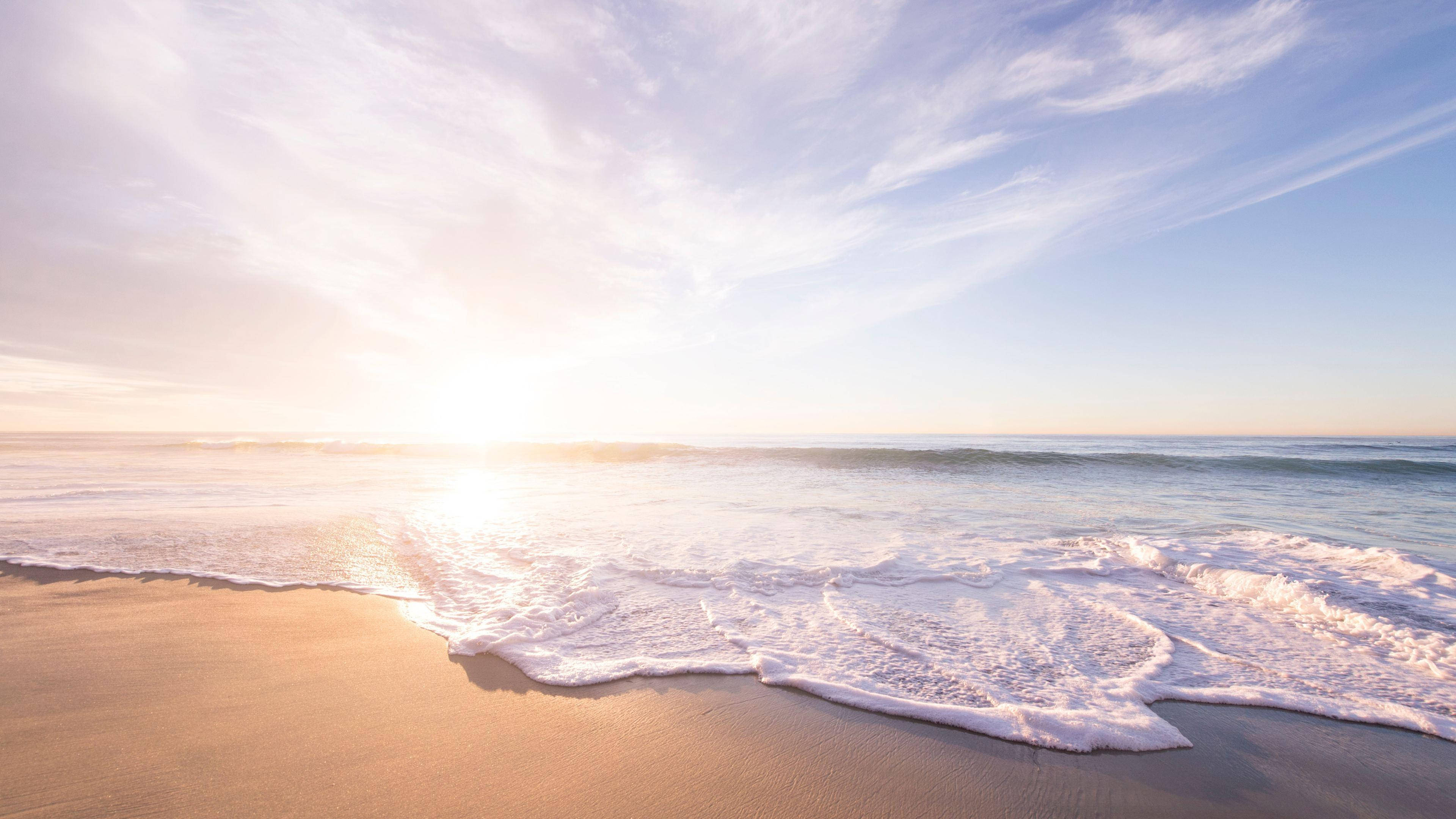 Beach Scenes Desktop 桌布 壁紙 — 金色日出將溫暖的光線投射在輕柔的海浪上，海浪在薄雲下滾滾湧上沙灘。