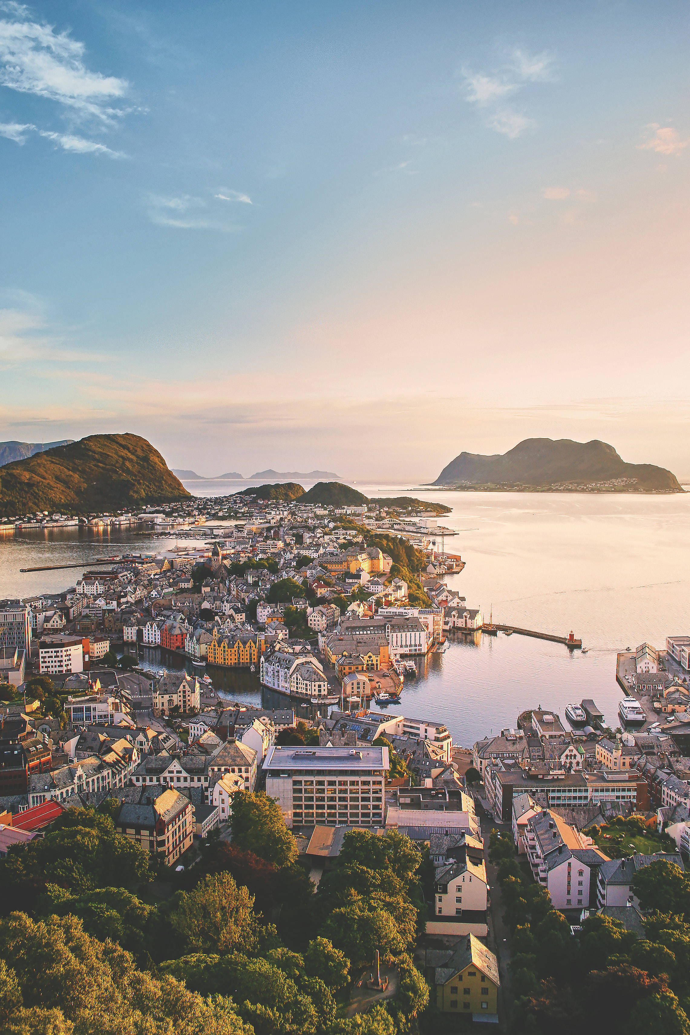 Norway 桌布 壁紙 — 金色日落時分，一個色彩繽紛的海岸小鎮坐落在翠綠山丘與平靜水域之間的鳥瞰圖。