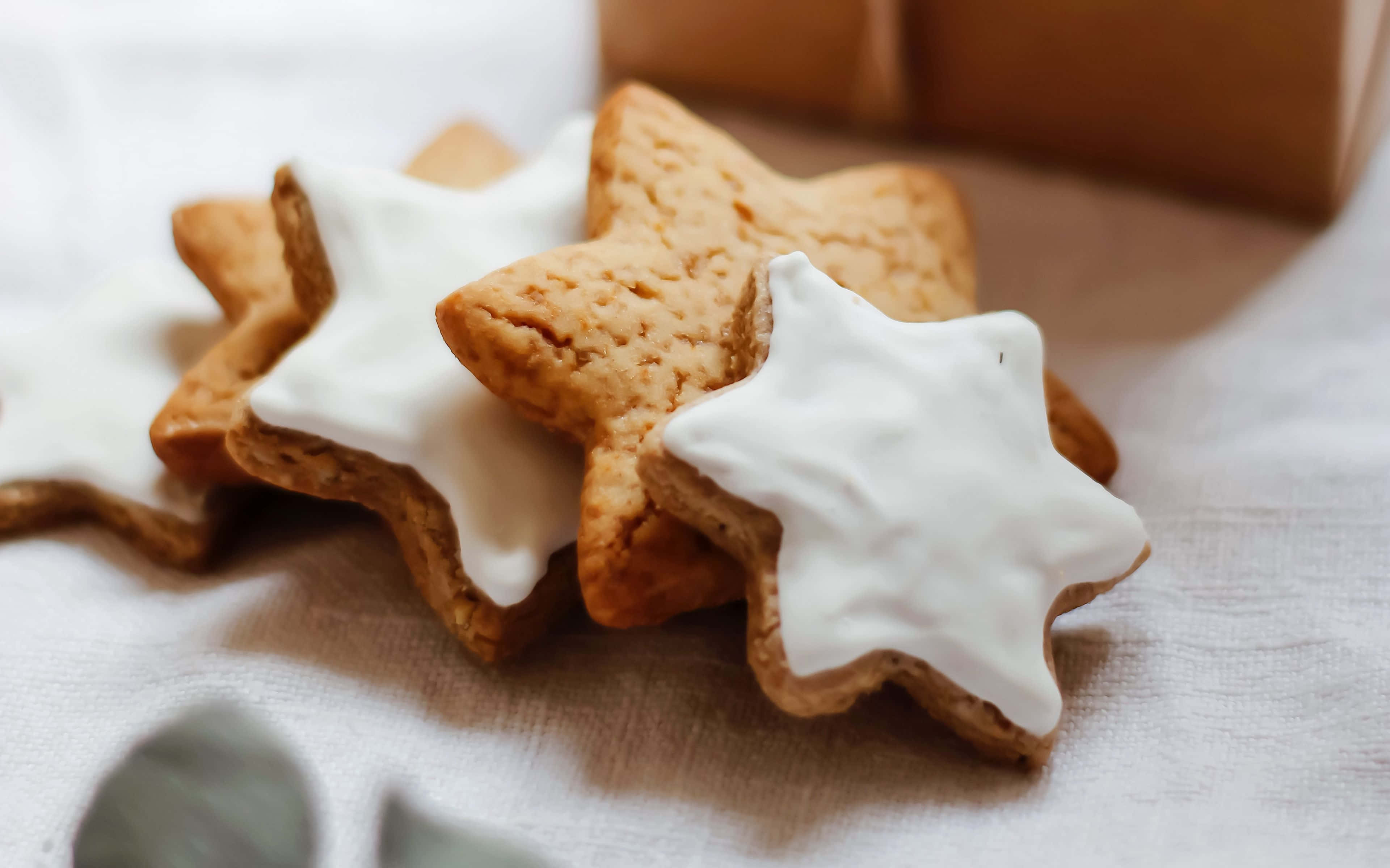 Cookies 桌布 壁紙 — 金色星形餅乾配上白色糖霜，放在柔軟的白布上，旁邊有一個棕色禮物盒。