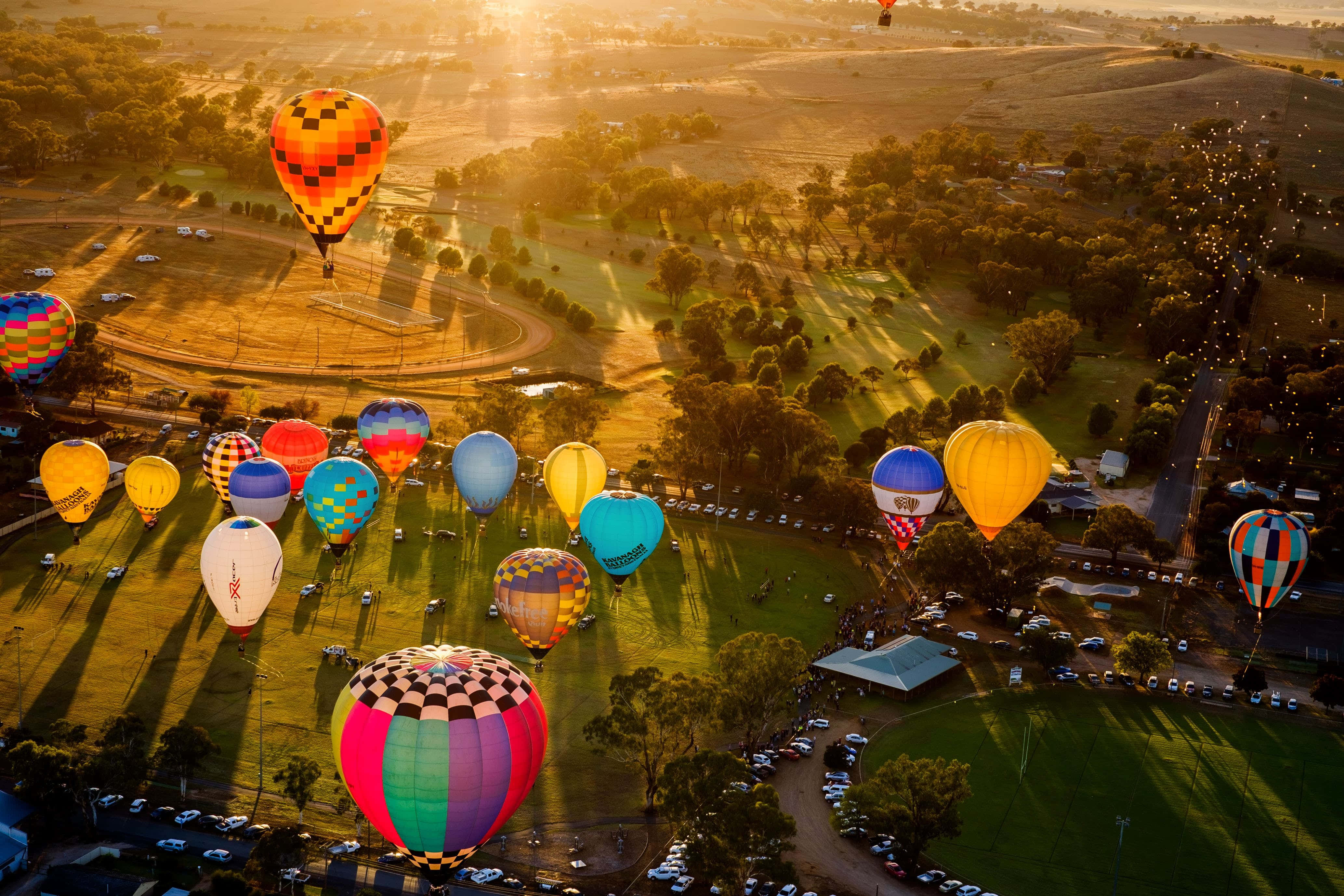 Hot Air Balloon 桌布 壁紙 — 金色時刻，陽光普照的草地上空飄浮著色彩繽紛的熱氣球的鳥瞰圖。