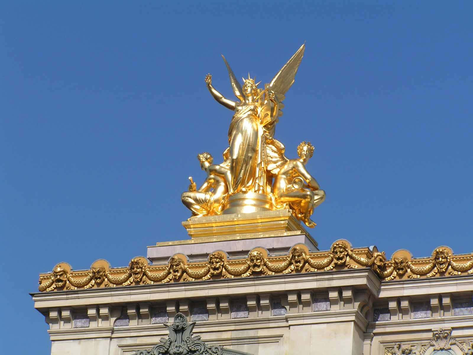 Statue Aesthetic 桌布 壁紙 — 金色有翼雕像矗立於宏偉的新古典主義建築頂端，襯托著清澈的藍天。