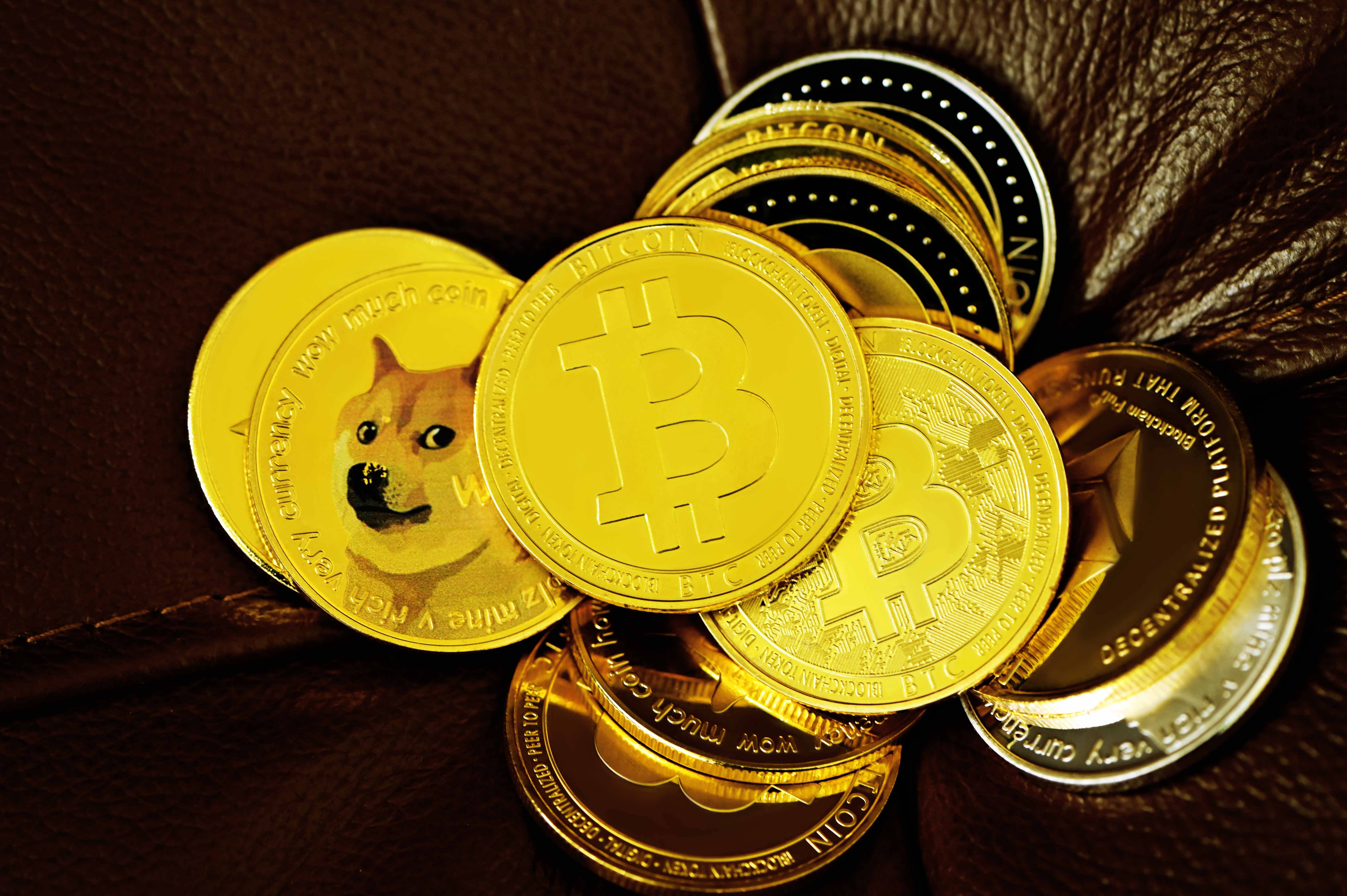 Dogecoin 桌布 壁紙 — 金色比特幣和狗狗幣代幣堆放在深棕色皮革上，配有溫暖的燈光。