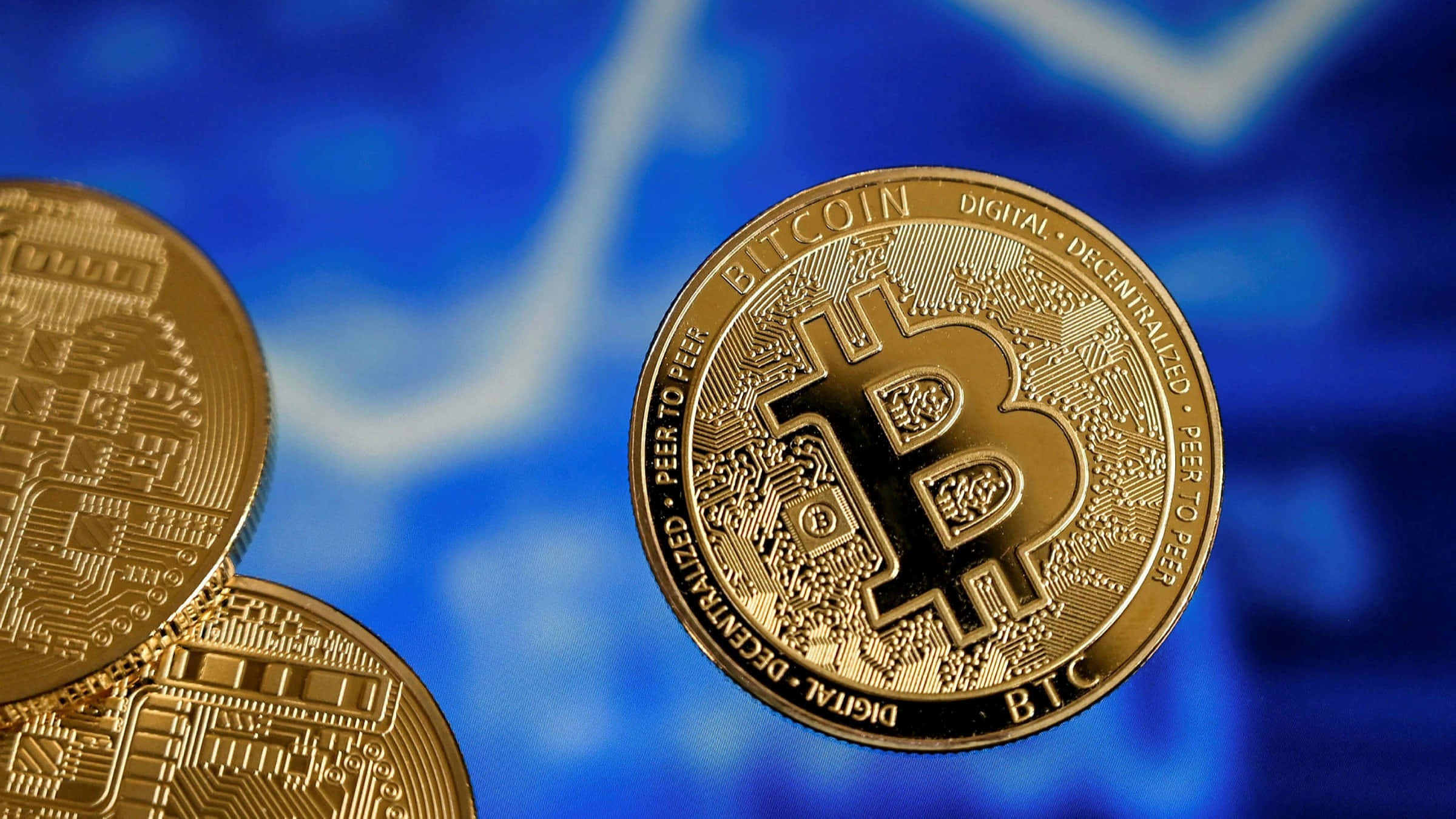 比特幣 桌布 壁紙 — 金色比特幣硬幣在模糊的藍色金融圖表背景上清晰對焦。