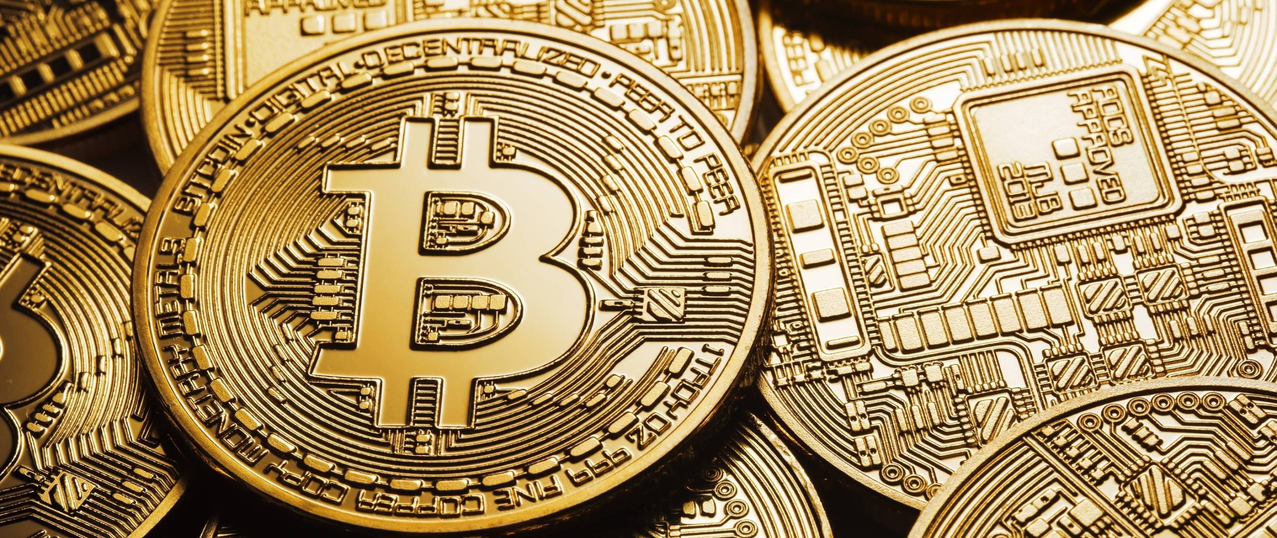 比特幣 桌布 壁紙 — 金色比特幣硬幣帶有電路板圖案，在溫暖燈光下於特寫堆疊中閃爍。
