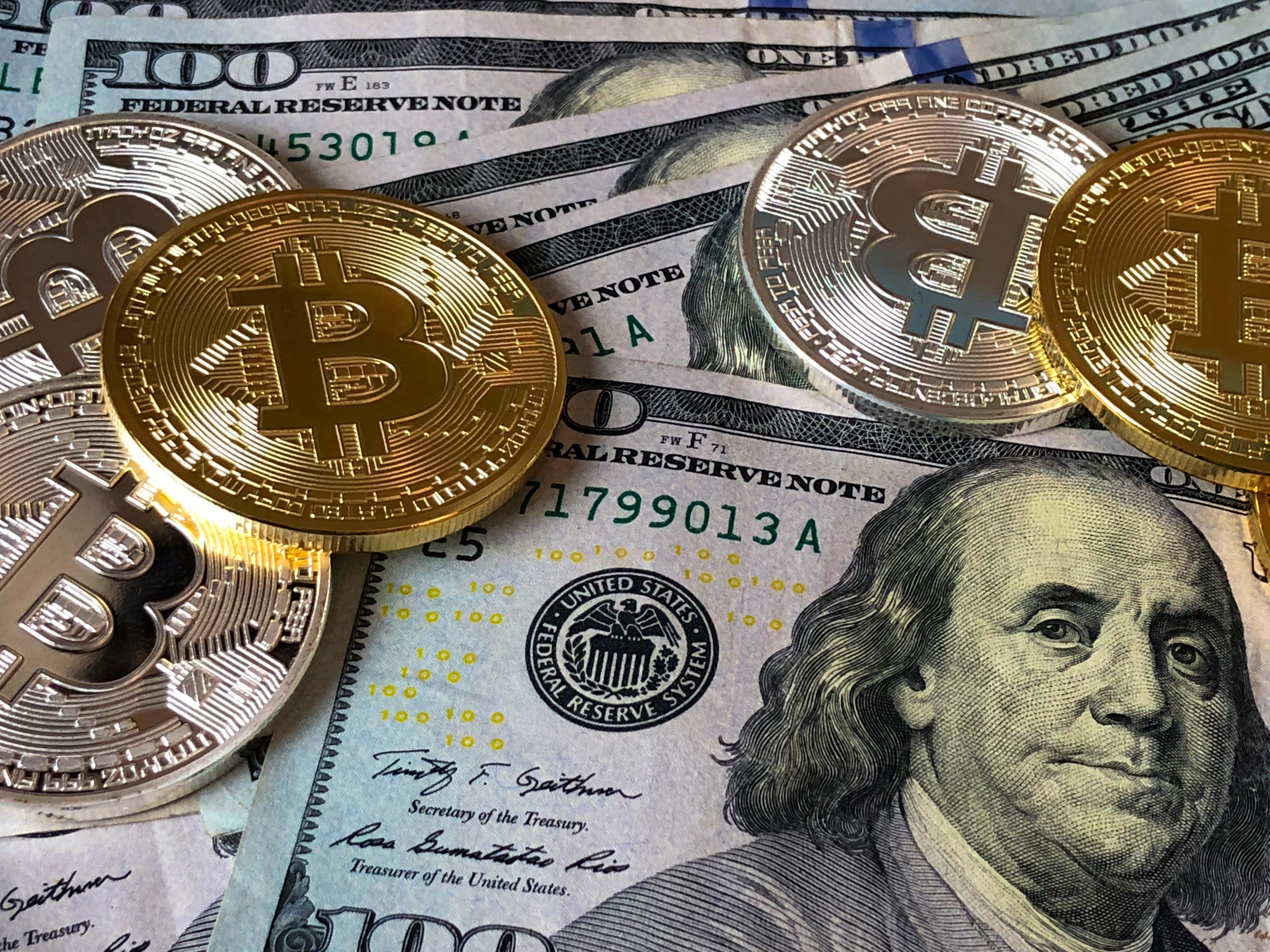 金錢 桌布 壁紙 — 金色比特幣硬幣放在一堆印有班傑明·富蘭克林肖像的100美元紙幣上。