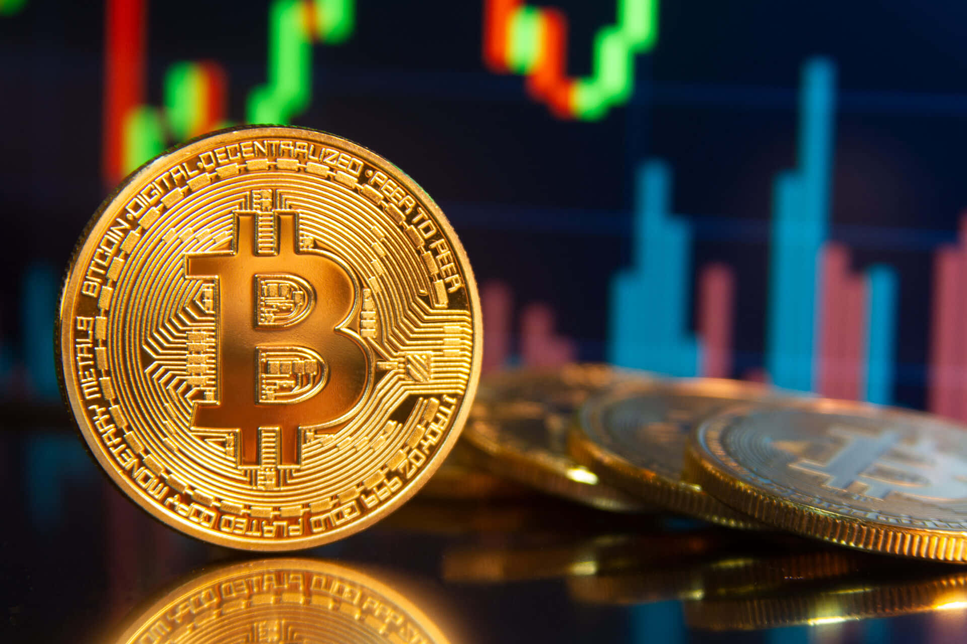 比特幣 桌布 壁紙 — 金色比特幣硬幣放在反光表面上，背景是模糊的股票圖表。