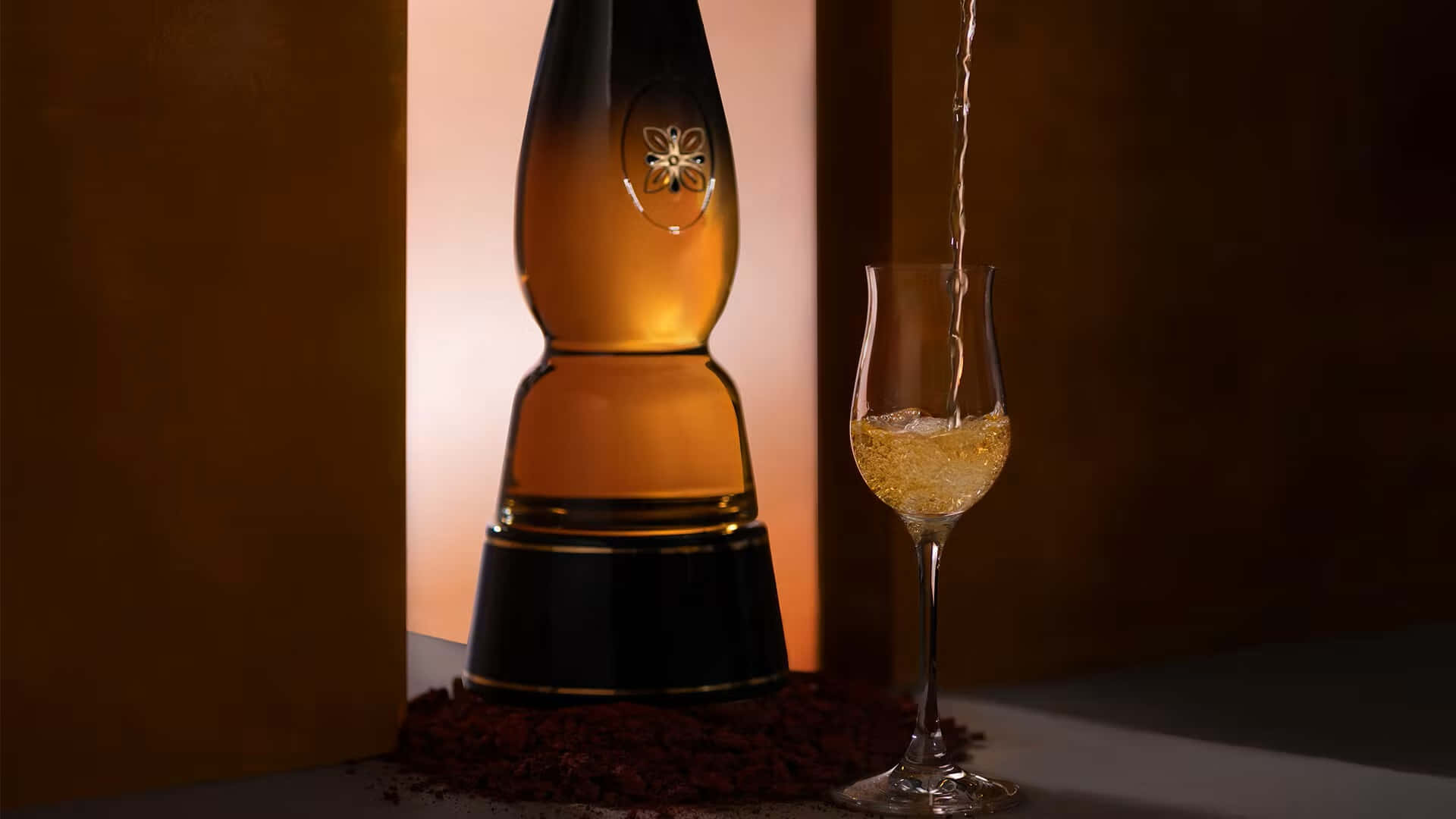 alcohol 桌布 壁紙 — 金色液體從優雅的瓶子倒入笛形杯，在溫暖的環境燈光下。