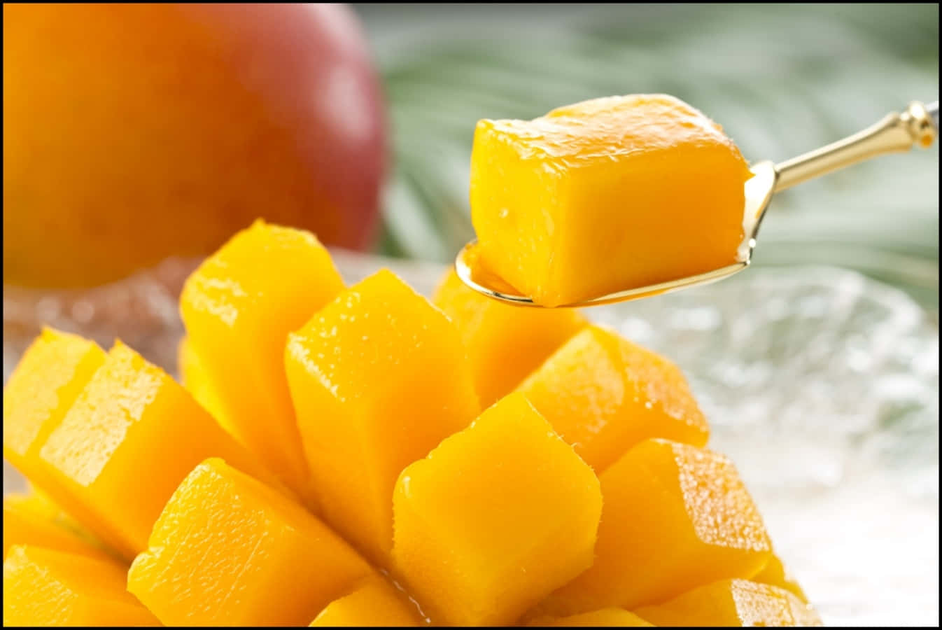 Mango 桌布 壁紙 — 金色湯匙將多汁芒果塊提起，置於一堆新鮮芒果塊之上。