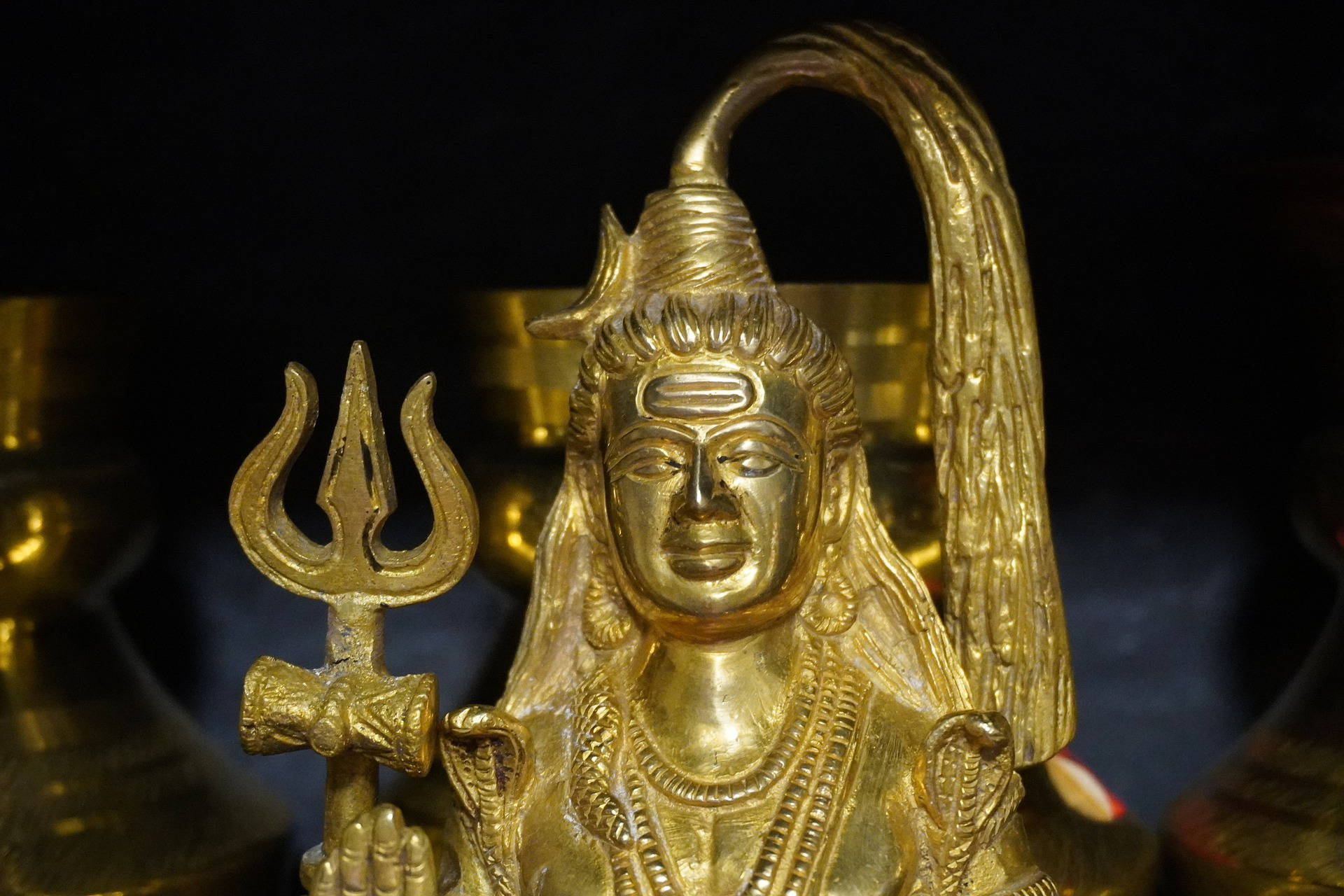 shiv shankar 桌布 壁紙 — 金色濕婆神像特寫，手持三叉戟，細節精緻，表情寧靜，背景深色。