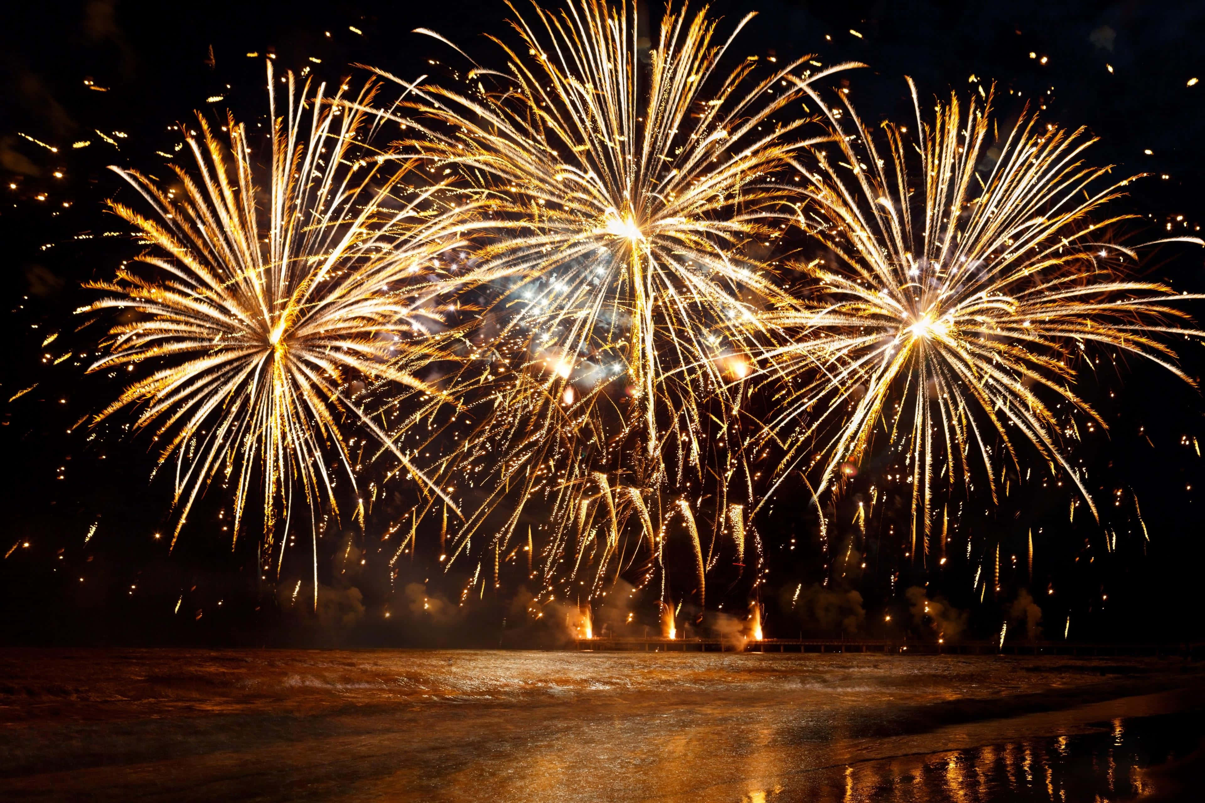 Fireworks 桌布 壁紙 — 金色煙火在夜晚的黑暗海洋上空綻放出耀眼的光芒，在水面上反射出燦爛的光輝。