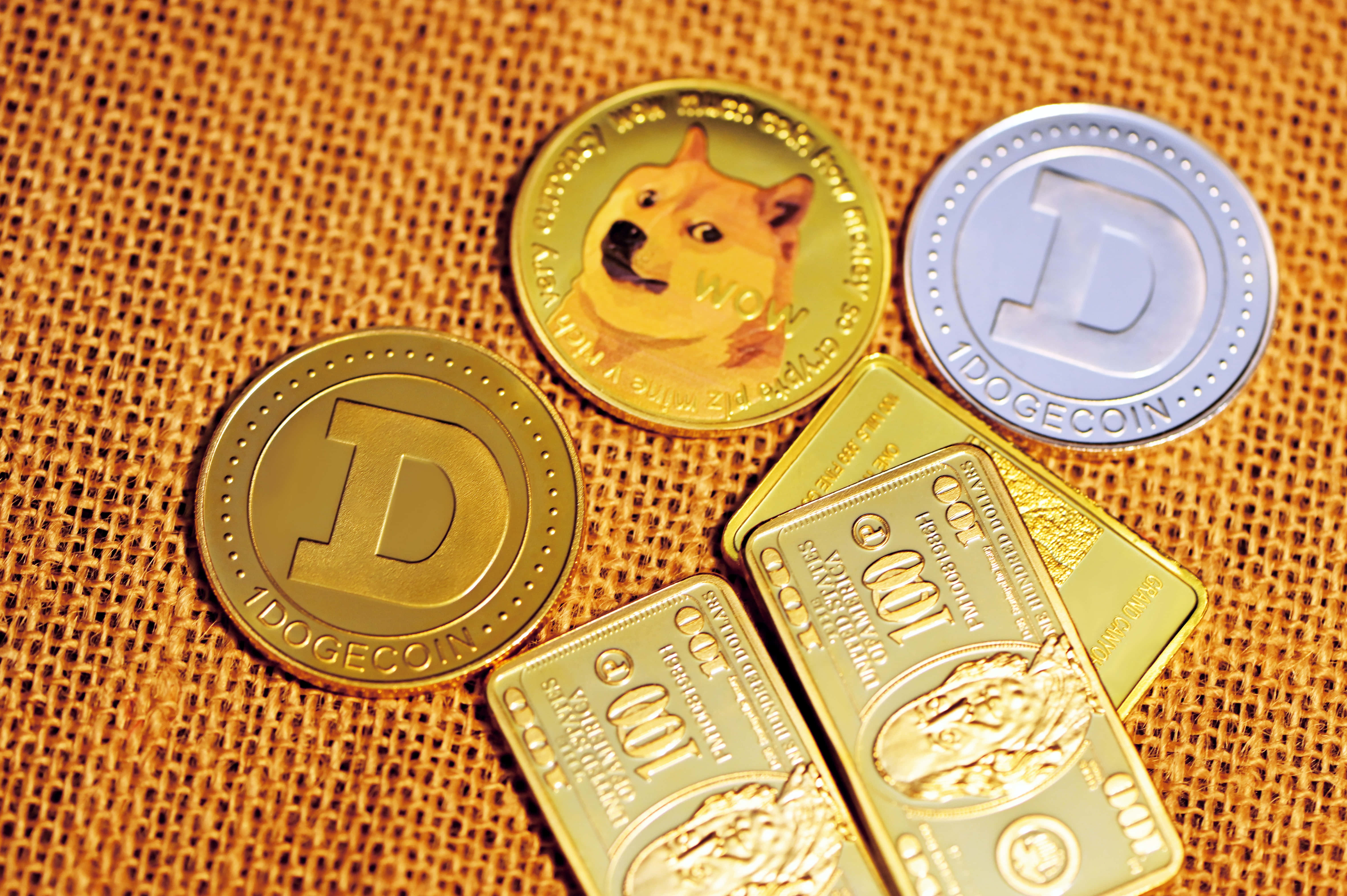 Dogecoin 桌布 壁紙 — 金色狗狗幣代幣和金條放在有紋理的粗麻布上，在溫暖的燈光下。