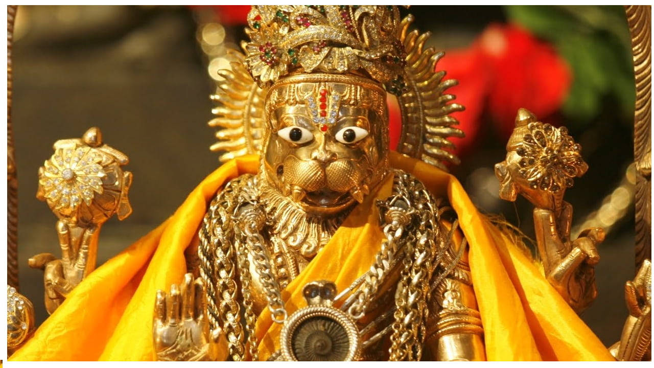Narasimha 桌布 壁紙 — 金色猴面神像，飾有珠寶和鏈條，披著鮮黃色布料。