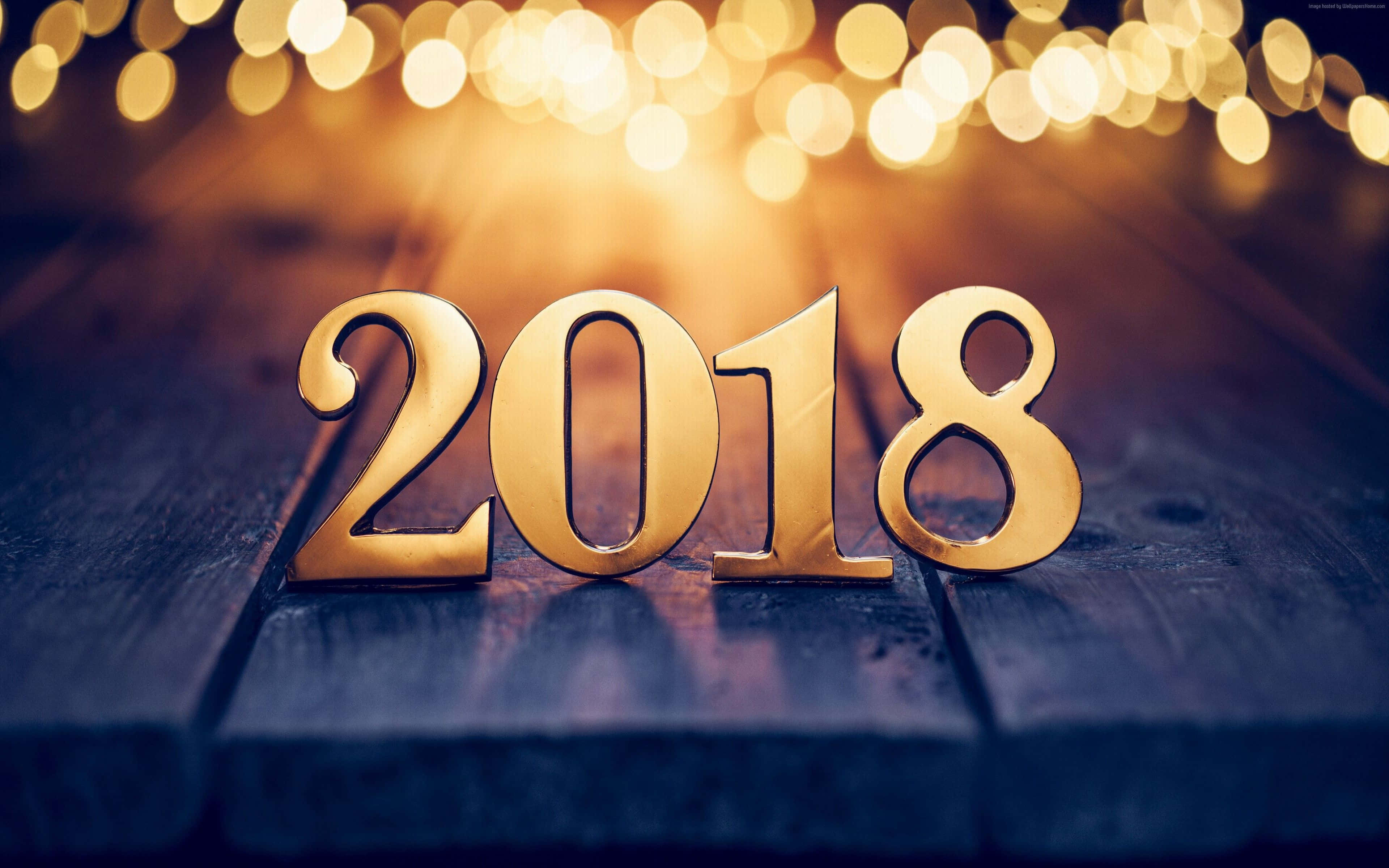 2018 桌布 壁紙 — 金色的2018數字放在深色木質表面上，背景有溫暖的散景燈光閃爍。