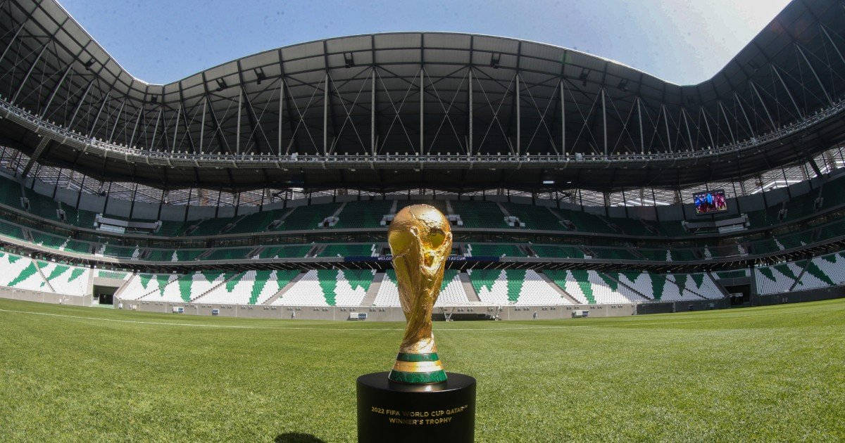 Qatar 桌布 壁紙 — 金色的FIFA世界盃獎盃在晴朗藍天下，矗立於廣闊空蕩體育館內充滿活力的綠色球場中央。