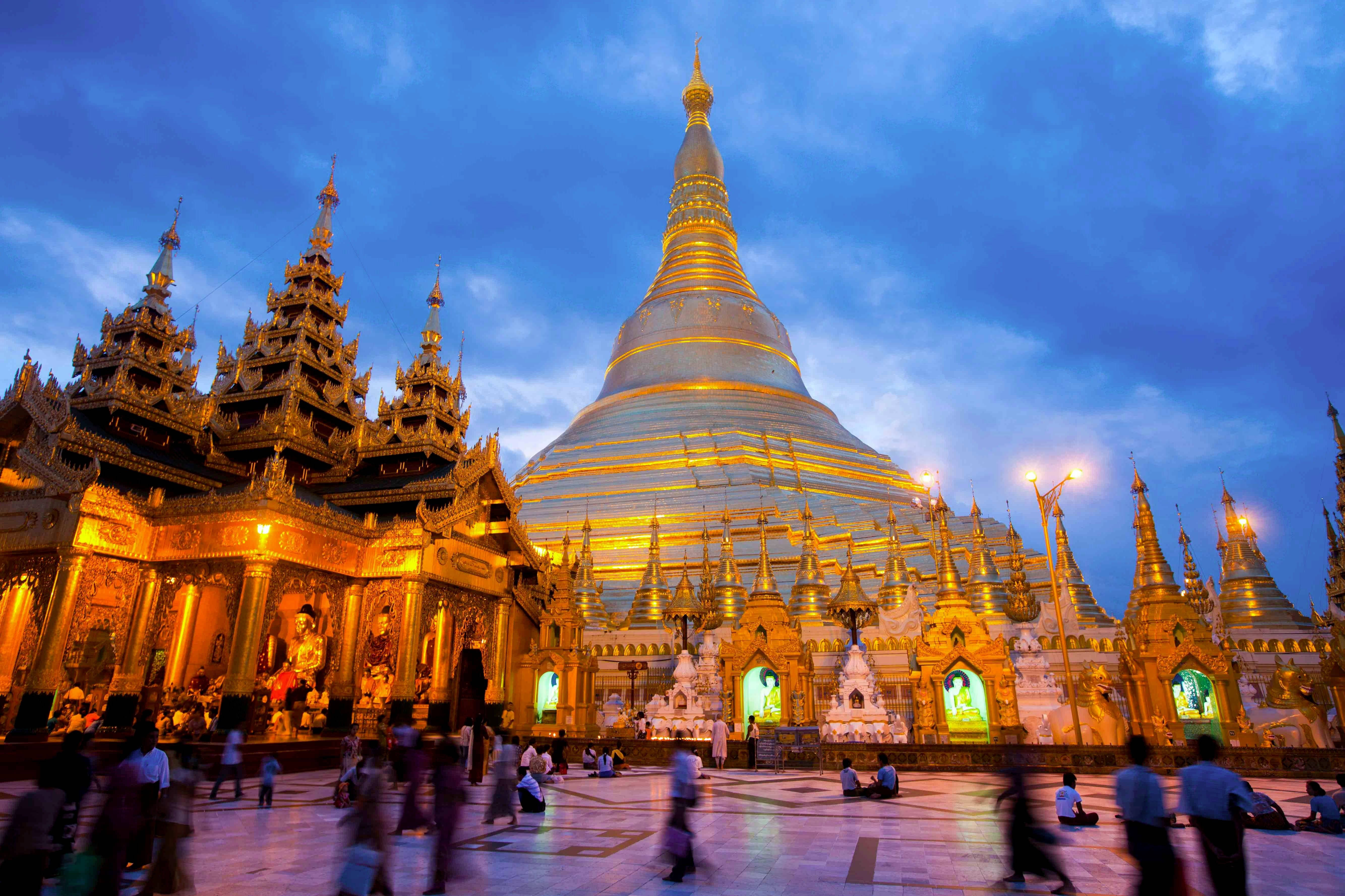 Burma 桌布 壁紙 — 金色的仰光雪德宮大金塔在深藍色的暮色天空下溫暖地發光，模糊的遊客在廣場上移動。