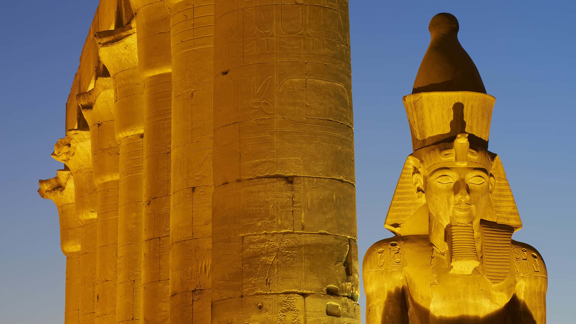 egyptian 桌布 壁紙 — 金色的埃及神廟柱子和獅身人面像在晴朗的藍天下沐浴在溫暖的日落光線中。