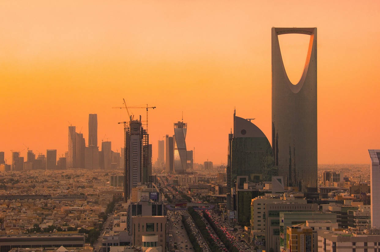 Riyadh 桌布 壁紙 — 金色的夕陽以溫暖的色調沐浴著利雅德的天際線，王國塔和周圍的摩天大樓在繁華的城市景觀之上聳立。