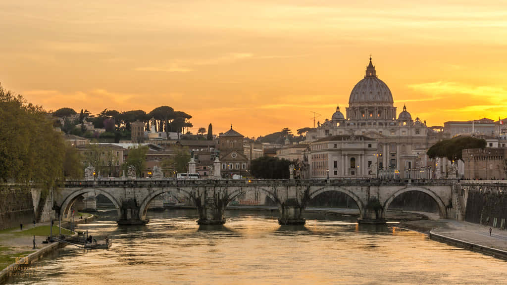 Italy Aesthetic 桌布 壁紙 — 金色的夕陽將台伯河和聖彼得大教堂沐浴在溫暖的光芒中，一座石橋優雅地拱跨在水面上。