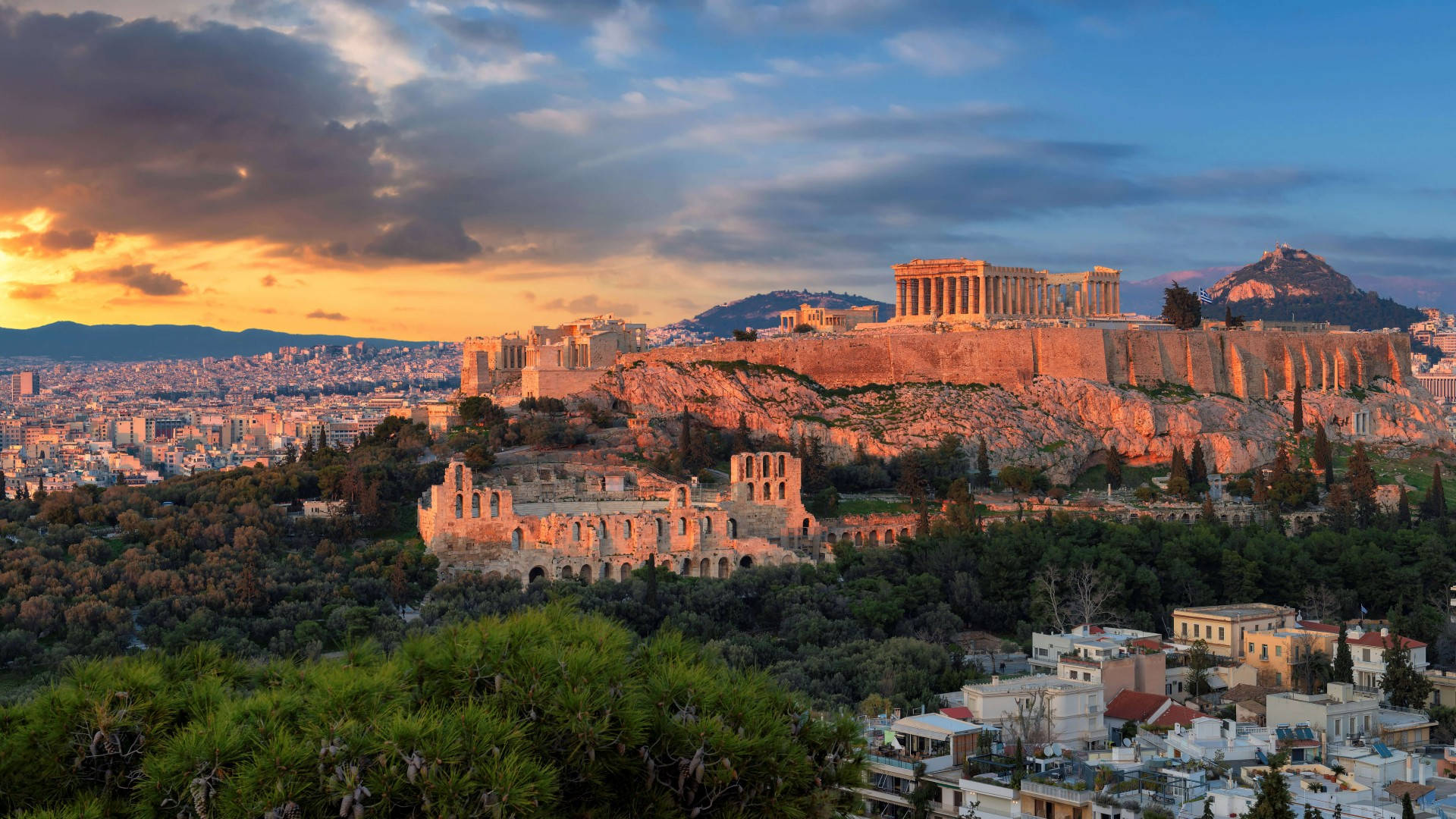 Athens 桌布 壁紙 — 金色的夕陽沐浴著古老的雅典衛城，溫暖的光芒下，現代城市景觀在下方延伸。