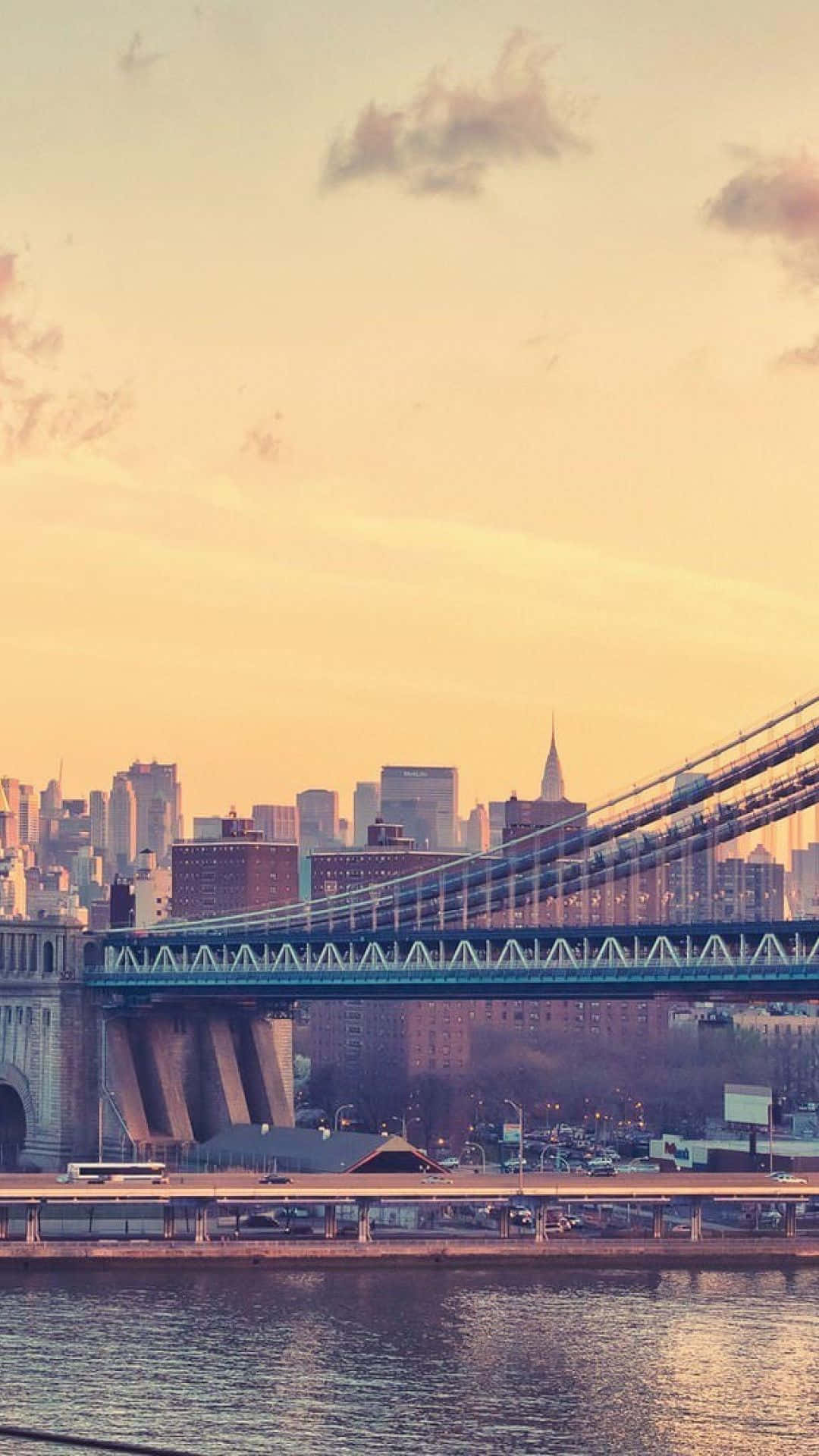 Android Ny City 桌布 壁紙 — 金色的夕陽沐浴著曼哈頓天際線和布魯克林大橋，溫暖的光線反射在下面的水面上。