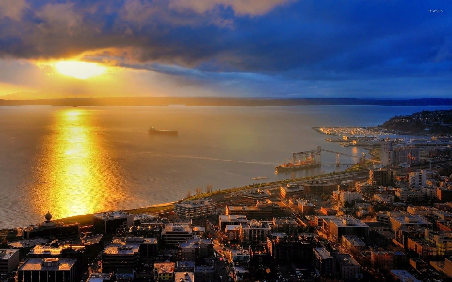 Seattle Washington 桌布 壁紙 — 金色的夕陽照耀著沿海城市景觀，一艘船在水上航行，雲朵投下戲劇性的陰影。