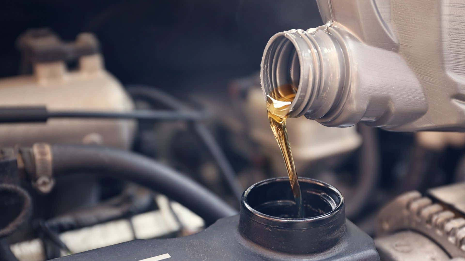 Oil 桌布 壁紙 — 金色的引擎機油從金屬瓶順暢地流入引擎的機油加註口，背景有模糊的機械部件。