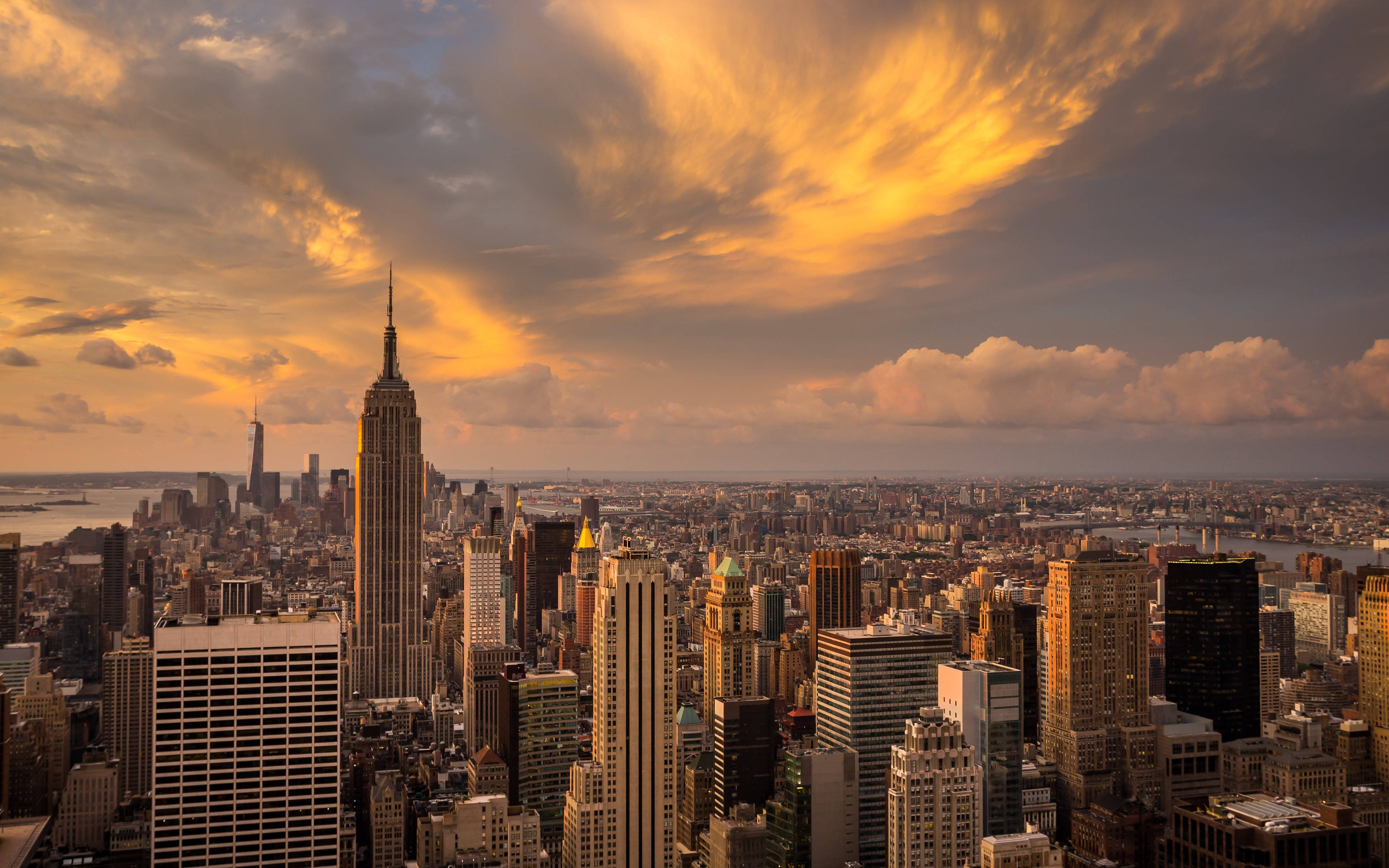 New York City Desktop 桌布 壁紙 — 金色的日落雲彩照亮了紐約市標誌性的天際線，帝國大廈高聳於密集的城市建築之上。