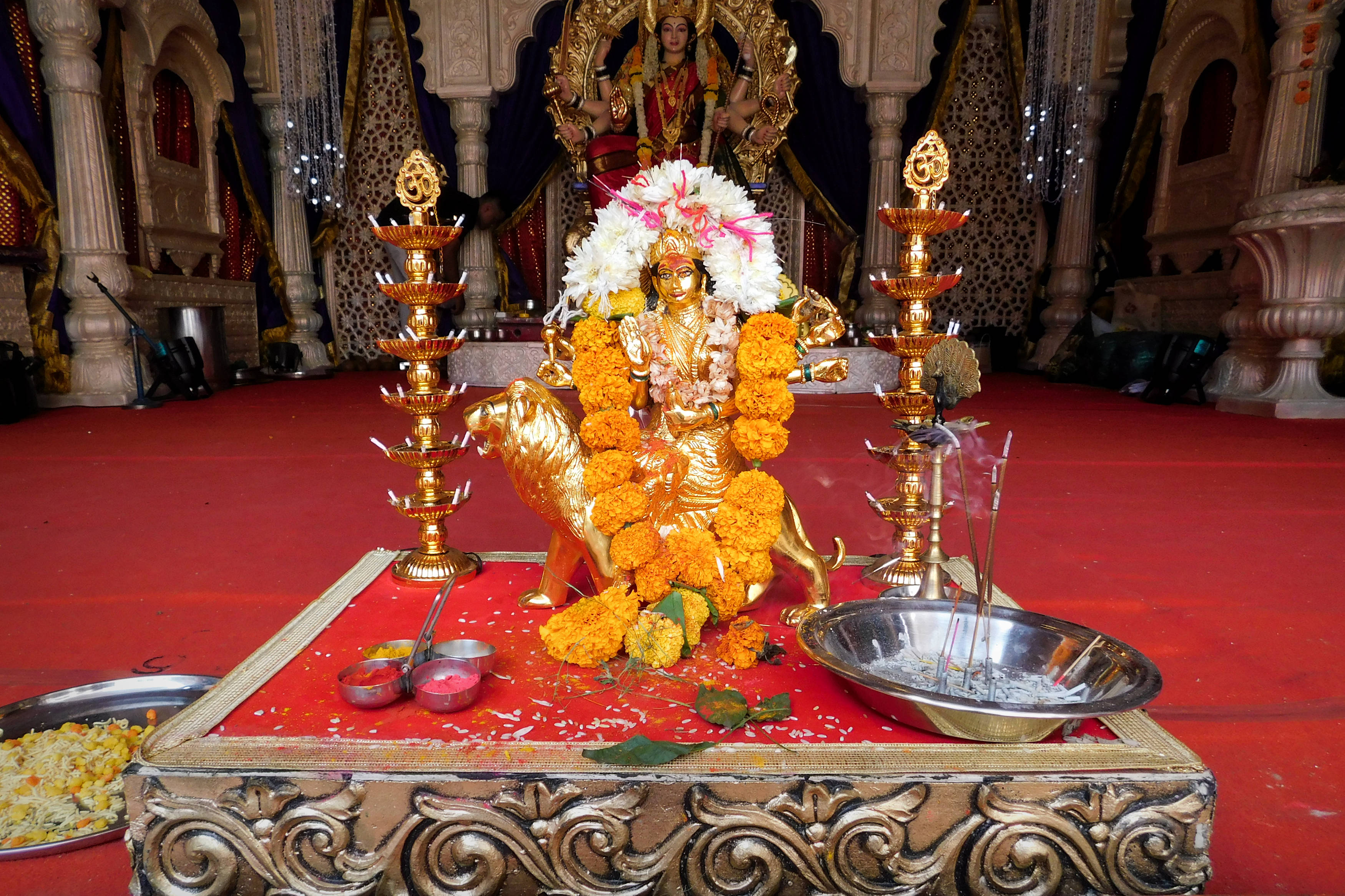 maa durga 桌布 壁紙 — 金色的杜爾迦女神像，用萬壽菊和白色鮮花裝飾，坐在華麗寺廟神龕的紅色平台上。