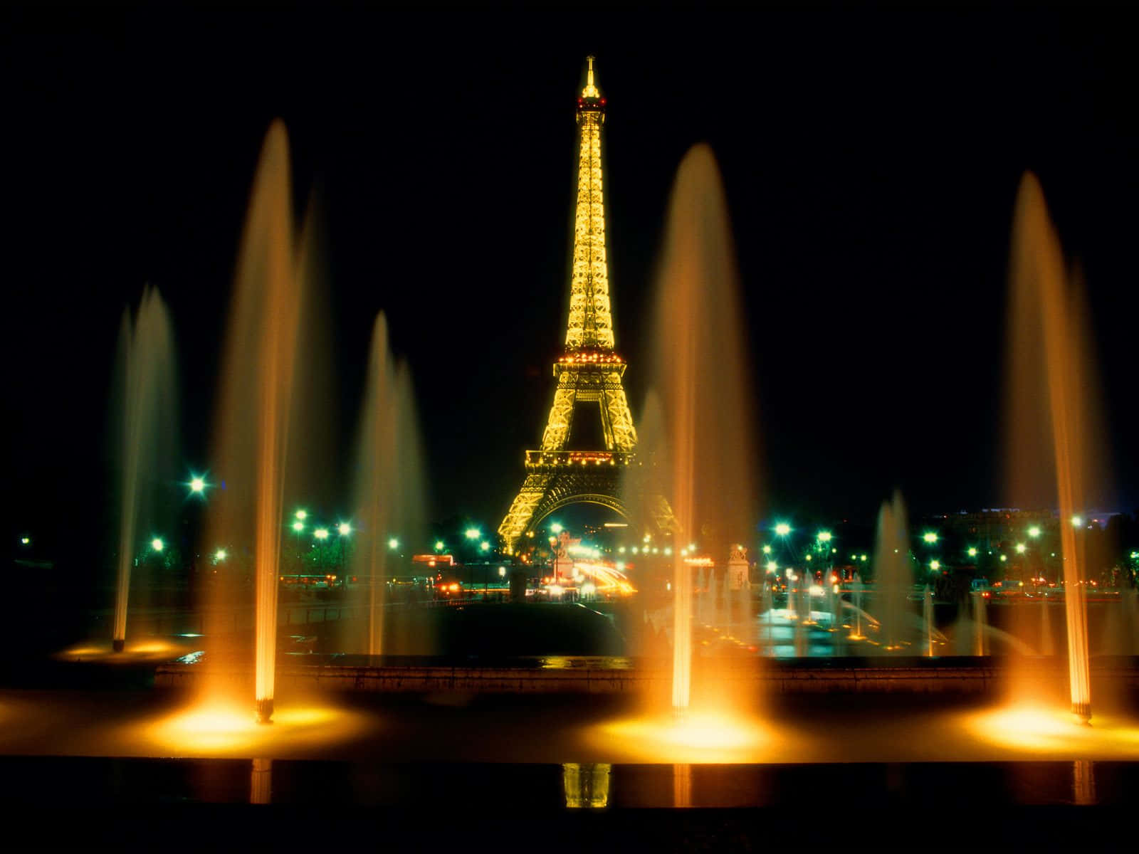 Eiffel Tower 桌布 壁紙 — 金色的艾菲爾鐵塔在夜晚於充滿活力的橙色噴泉後方發光。