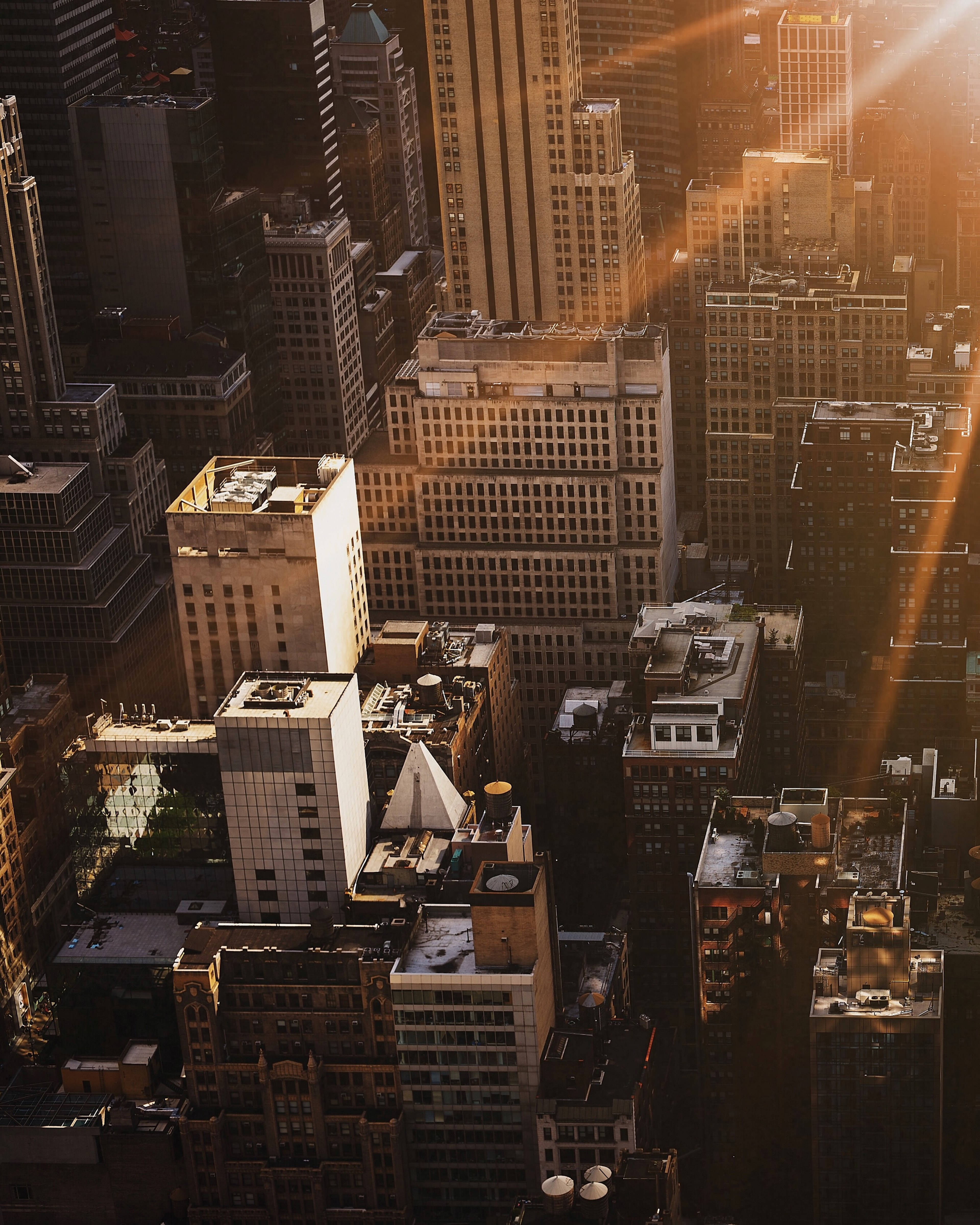 Buildings 桌布 壁紙 — 金色的陽光穿過高聳的摩天大樓，在日落時分將戲劇性的光線投射在密集的城市峽谷中。