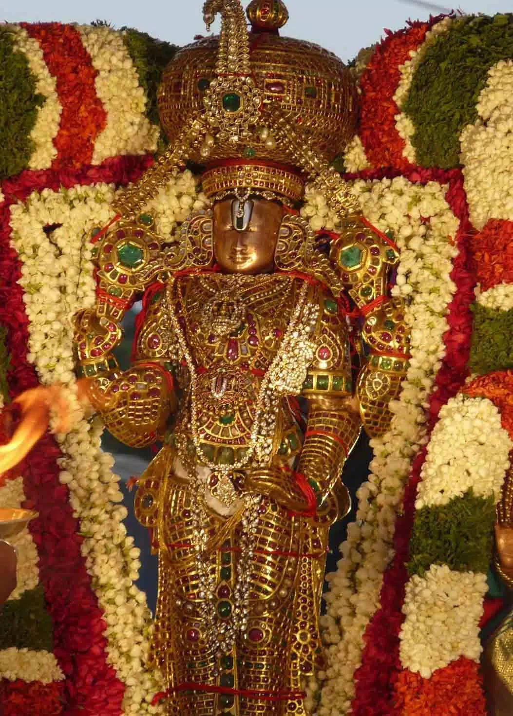 lord venkateswara HD 桌布 壁紙 — 金色神像，飾以精緻珠寶，周圍環繞著鮮豔的紅、白、綠色花環。