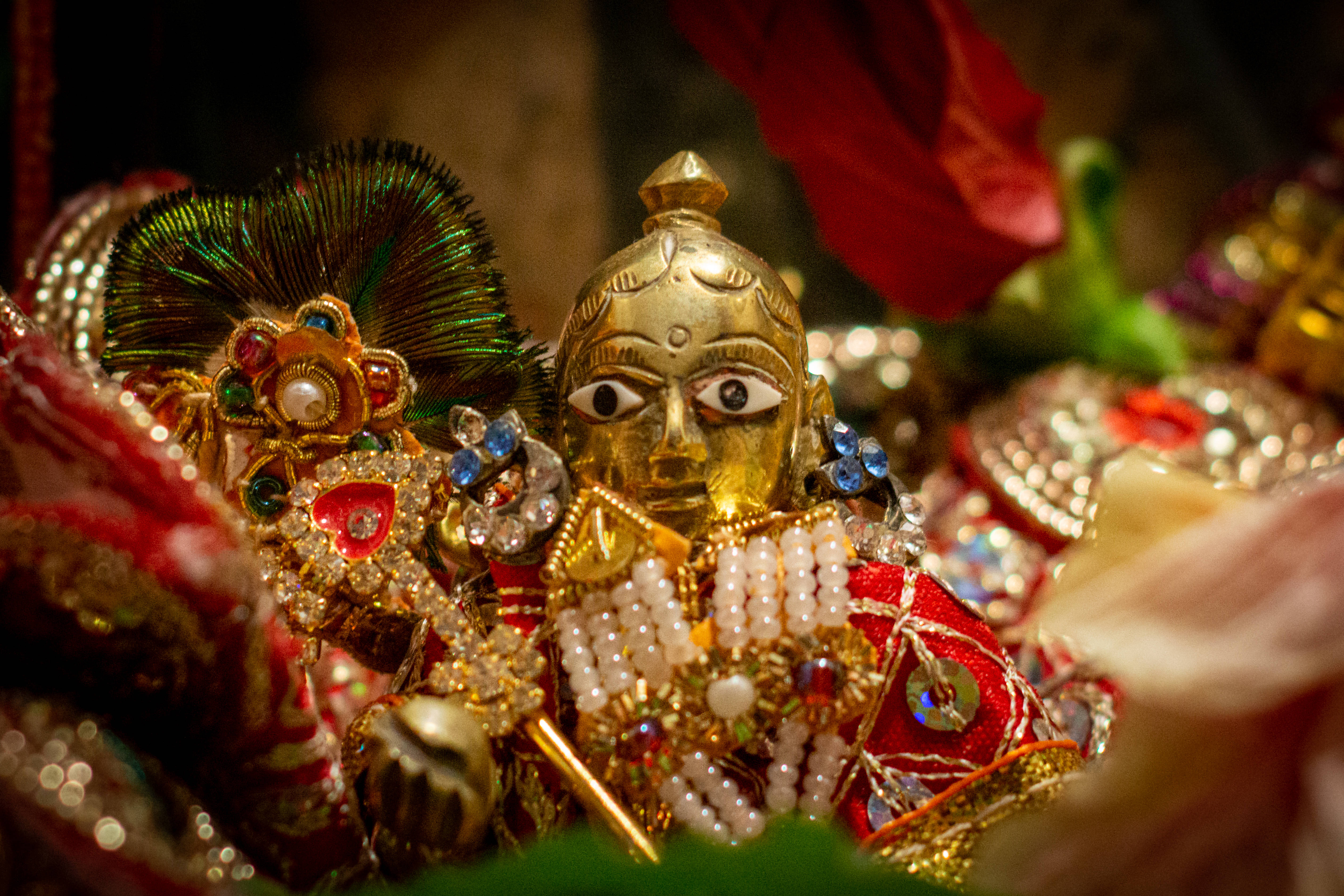 Gopal 桌布 壁紙 — 金色神像的特寫，飾有珠寶、珍珠和紅色布料，背景是暗色模糊的。