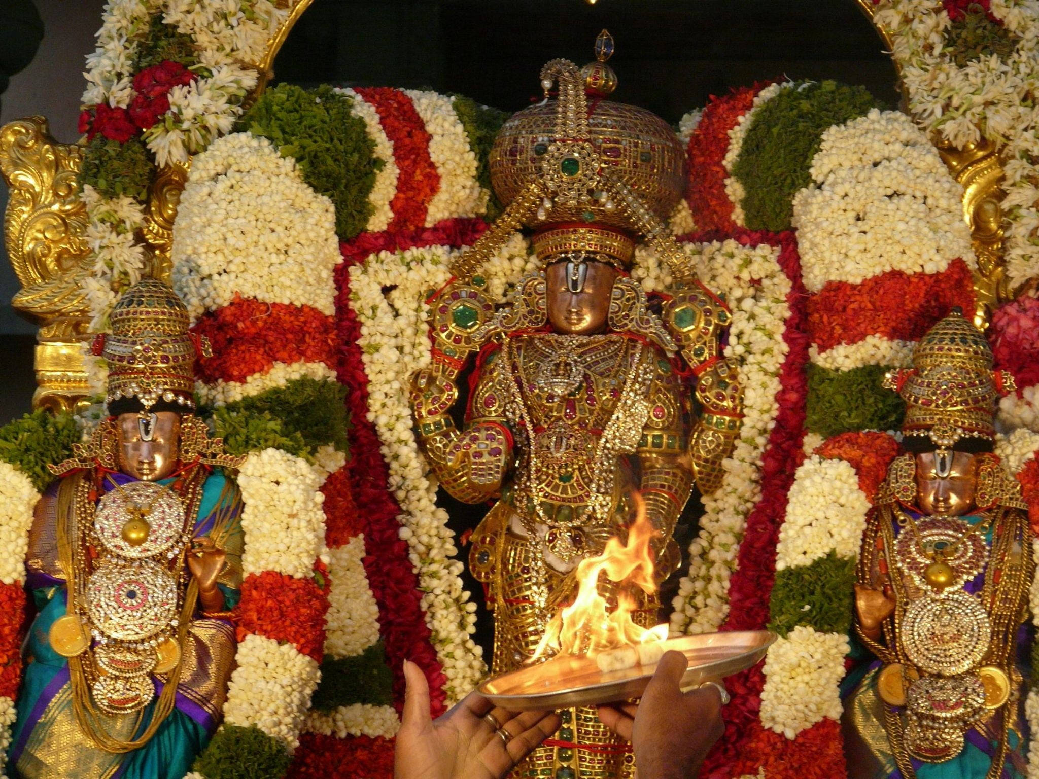 Venkateswara 桌布 壁紙 — 金色神像飾以紅、白、綠色花環，雙手在前方奉上點亮的燈。