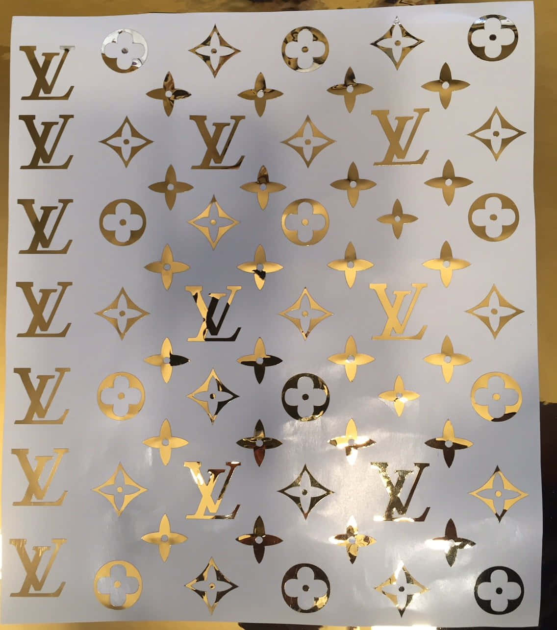 Louis Vuitton Pattern 桌布 壁紙 — 金色箔紙Louis Vuitton字母組合貼紙，帶有LV標誌和花卉圖案，白色底紙。
