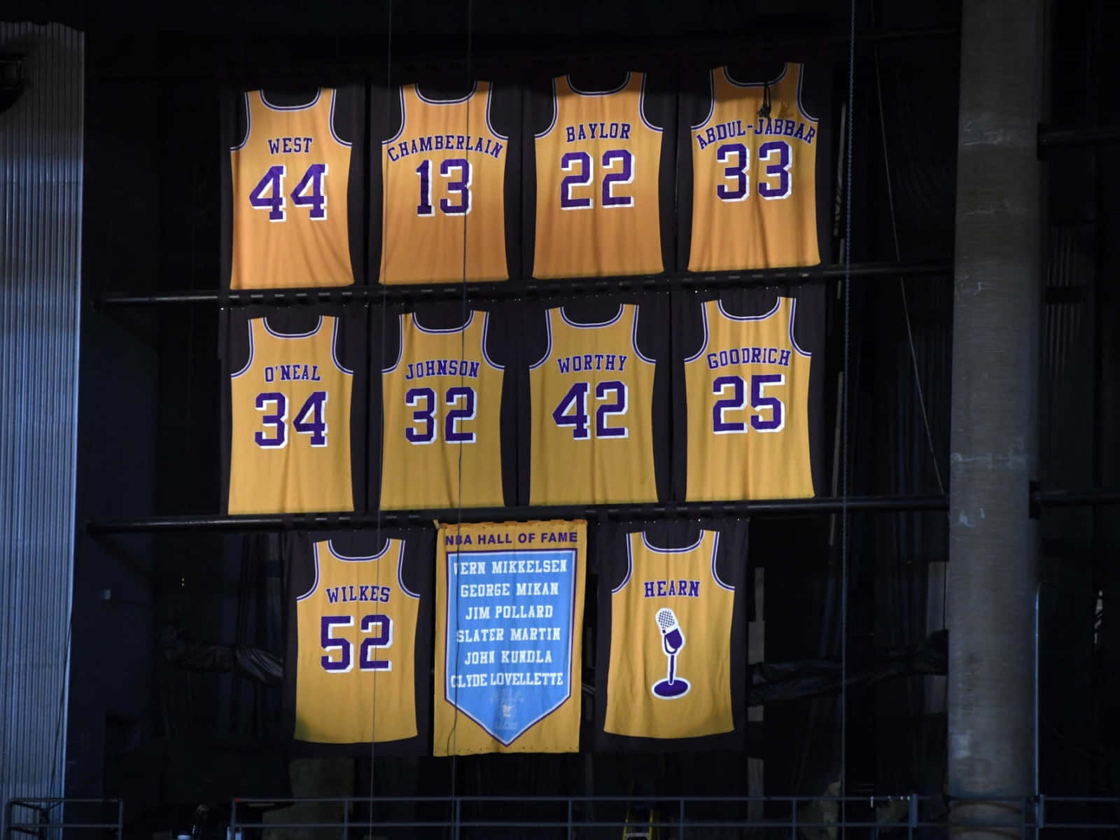 NBA 桌布 壁紙 — 金色籃球球衣上印有球員姓名和號碼，懸掛在燈光昏暗的博物館展覽中。