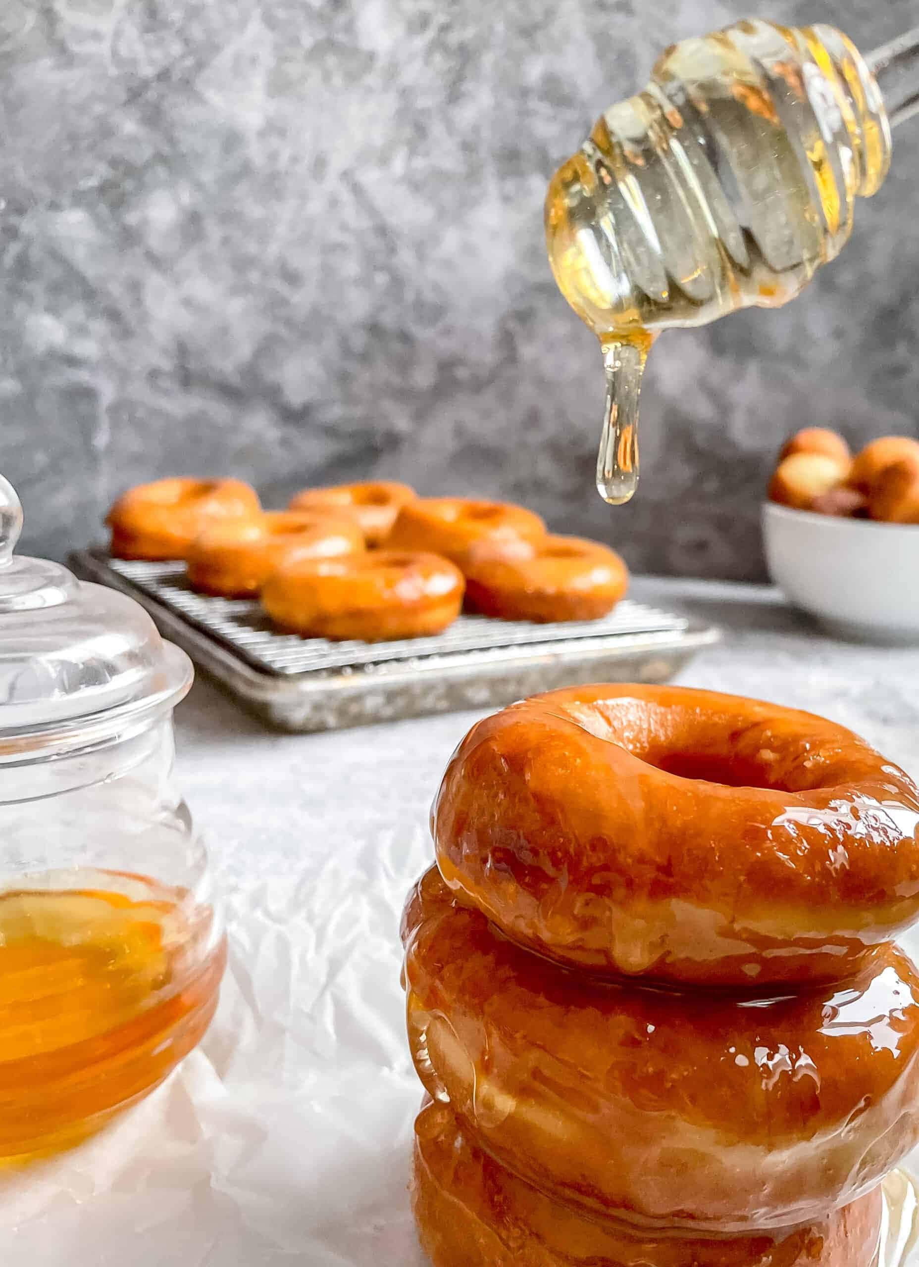Glazed Donut 桌布 壁紙 — 金色糖霜甜甜圈高高疊起，蜂蜜從木勺滴落，背景為灰色大理石。