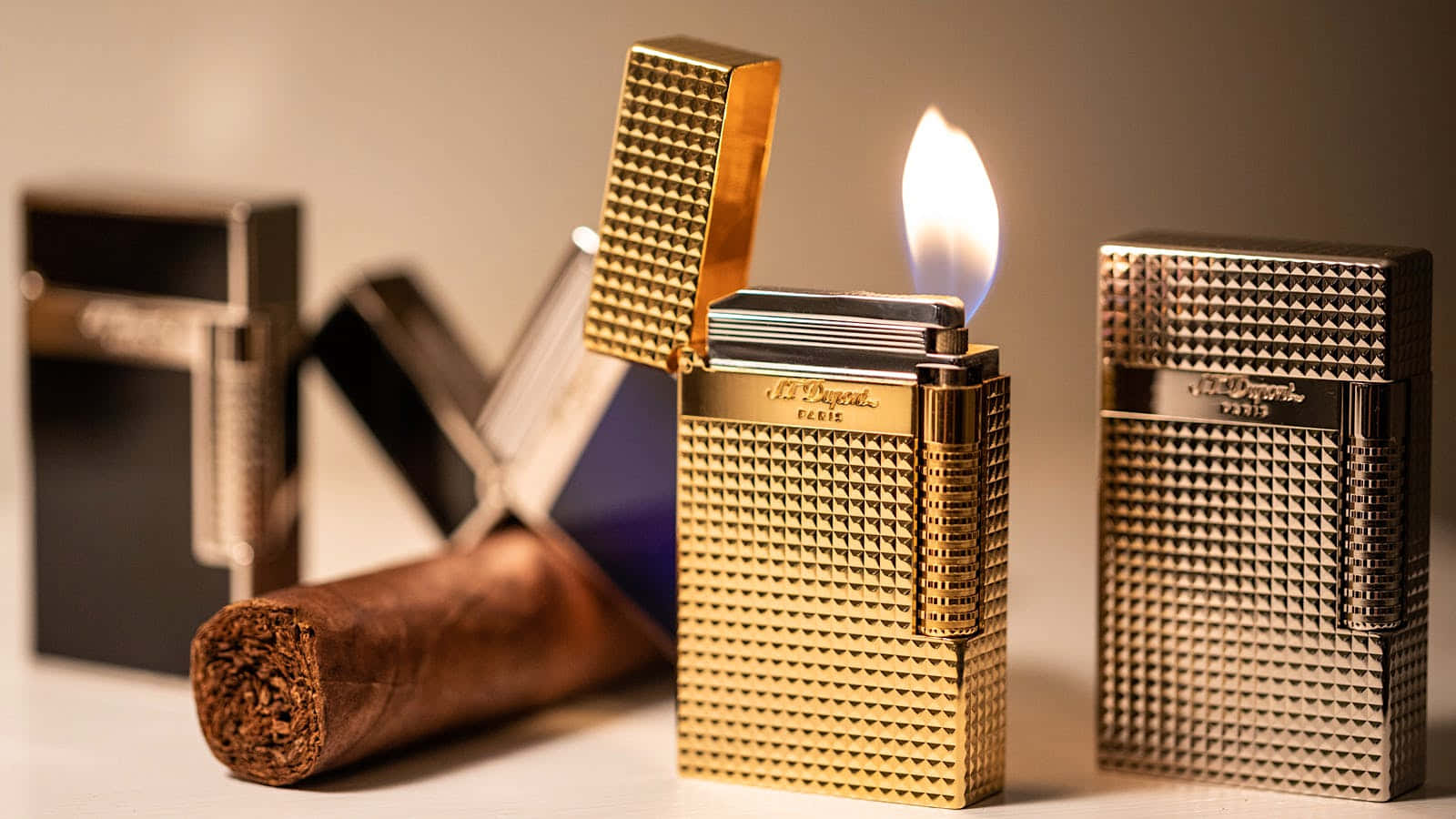 lighter 桌布 壁紙 — 金色紋理打火機在極簡表面上點燃火焰，旁邊有深色雪茄和時尚金屬打火機。