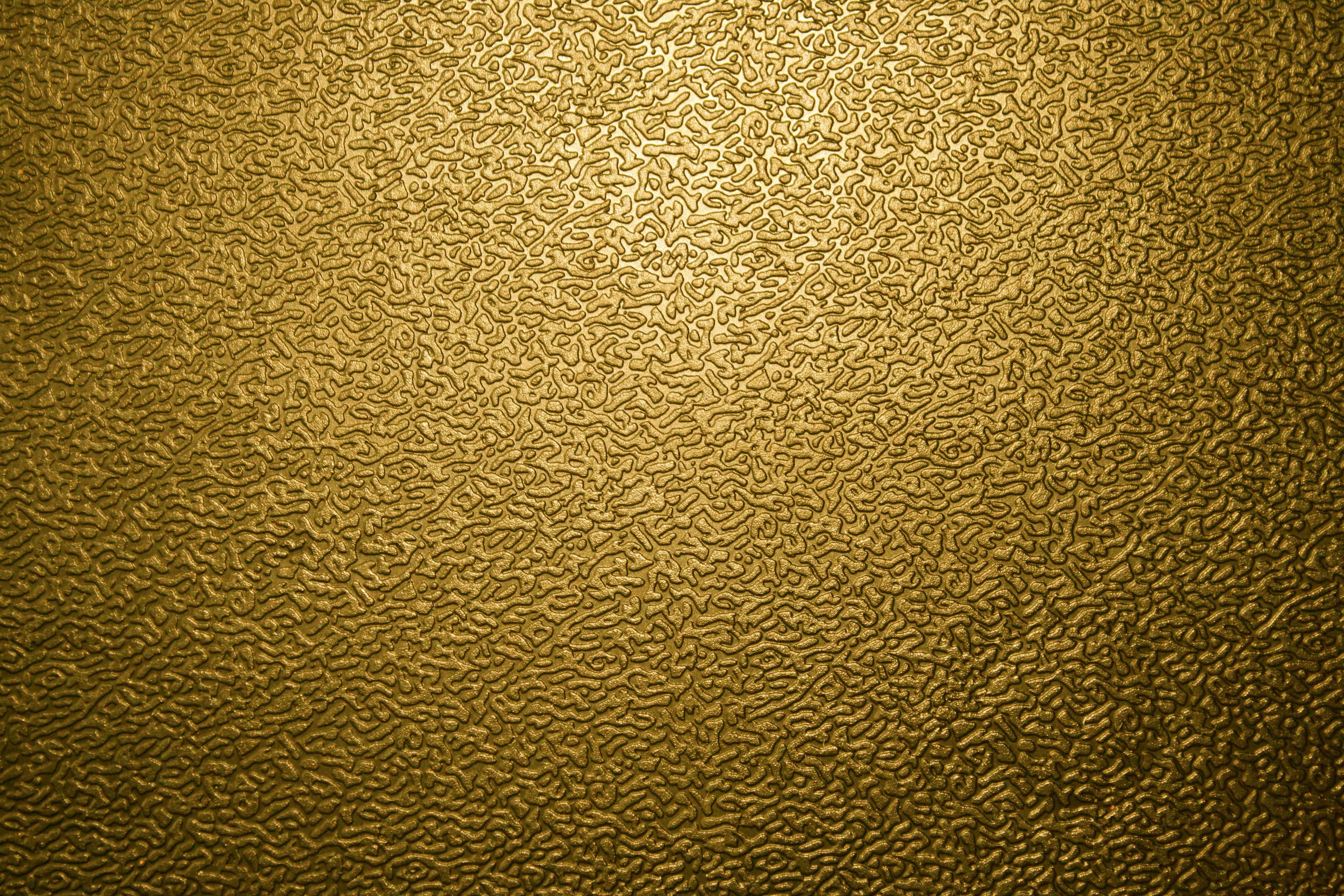Metallic Gold 桌布 壁紙 — 金色紋理表面，帶有漩渦狀浮雕圖案，由柔和漸變燈光照亮。