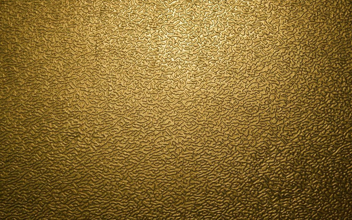 Metallic Gold 桌布 壁紙 — 金色紋理表面，帶有漩渦狀浮雕圖案，由柔和漸變照明照亮。