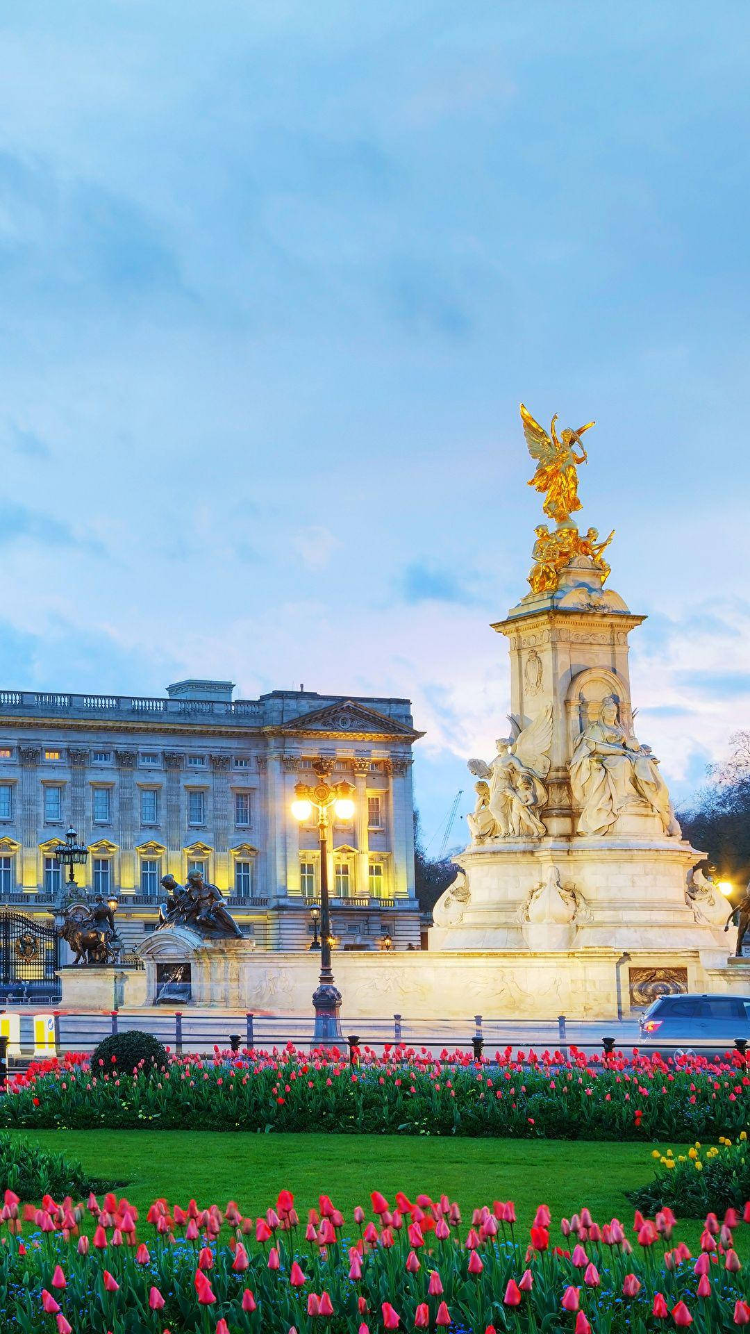 England 桌布 壁紙 — 金色維多利亞紀念碑在黃昏時分於白金漢宮旁閃耀，前景有粉紅色鬱金香。