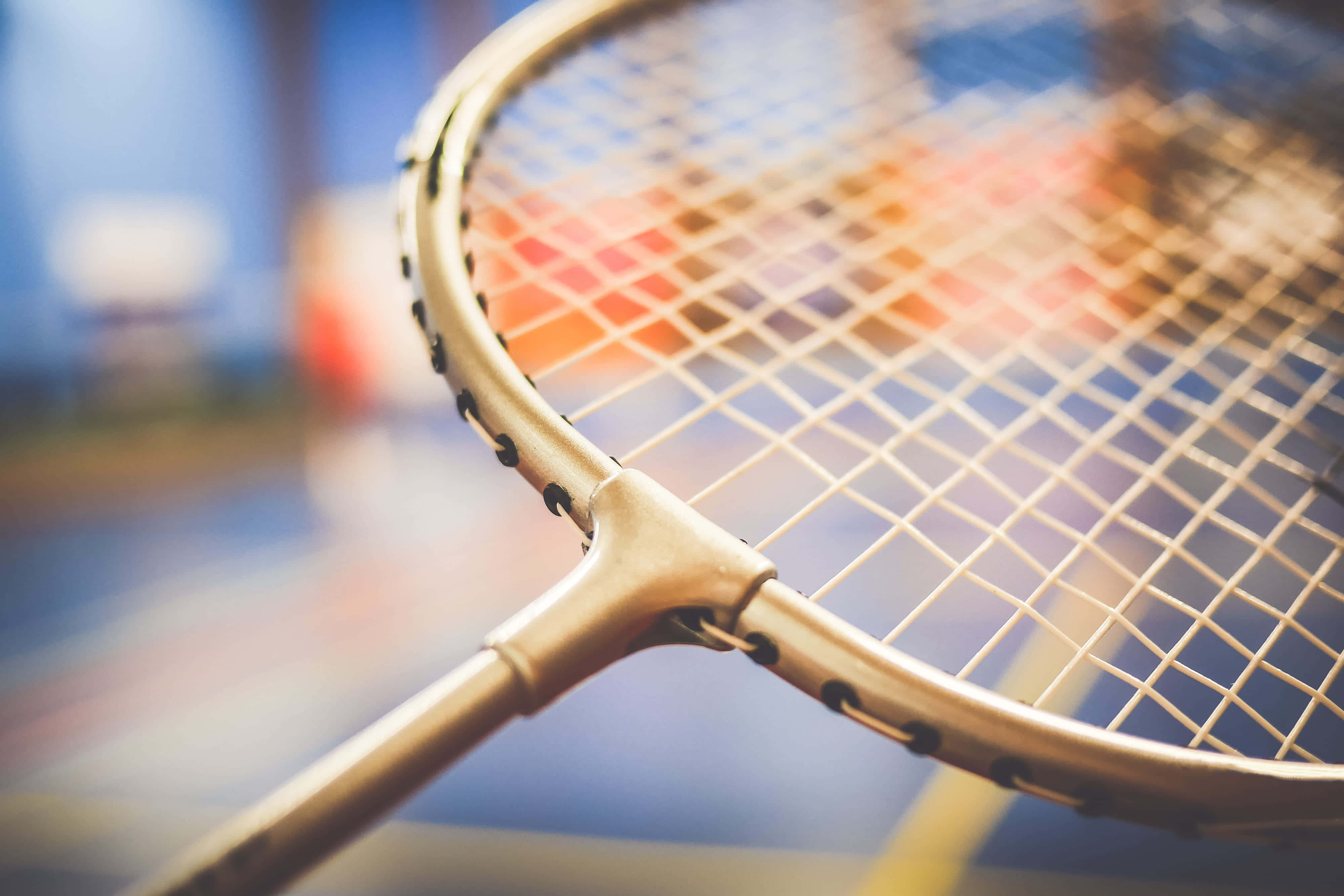 Badminton 桌布 壁紙 — 金色網球拍的近距離特寫，帶有詳細的網線，背景是模糊多彩的球場。